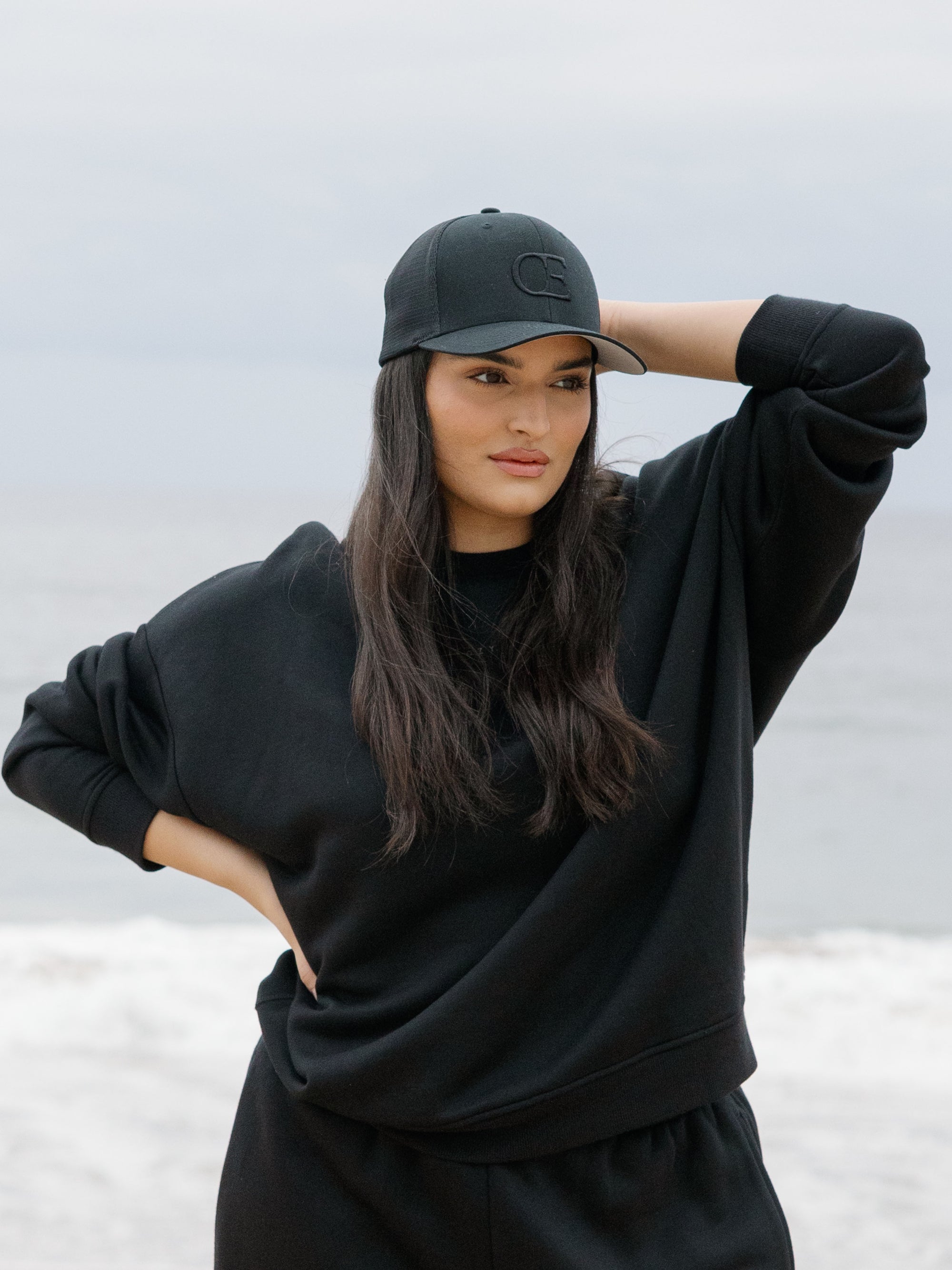 Woman wearing a black cap with a CE logo on a light gray background 