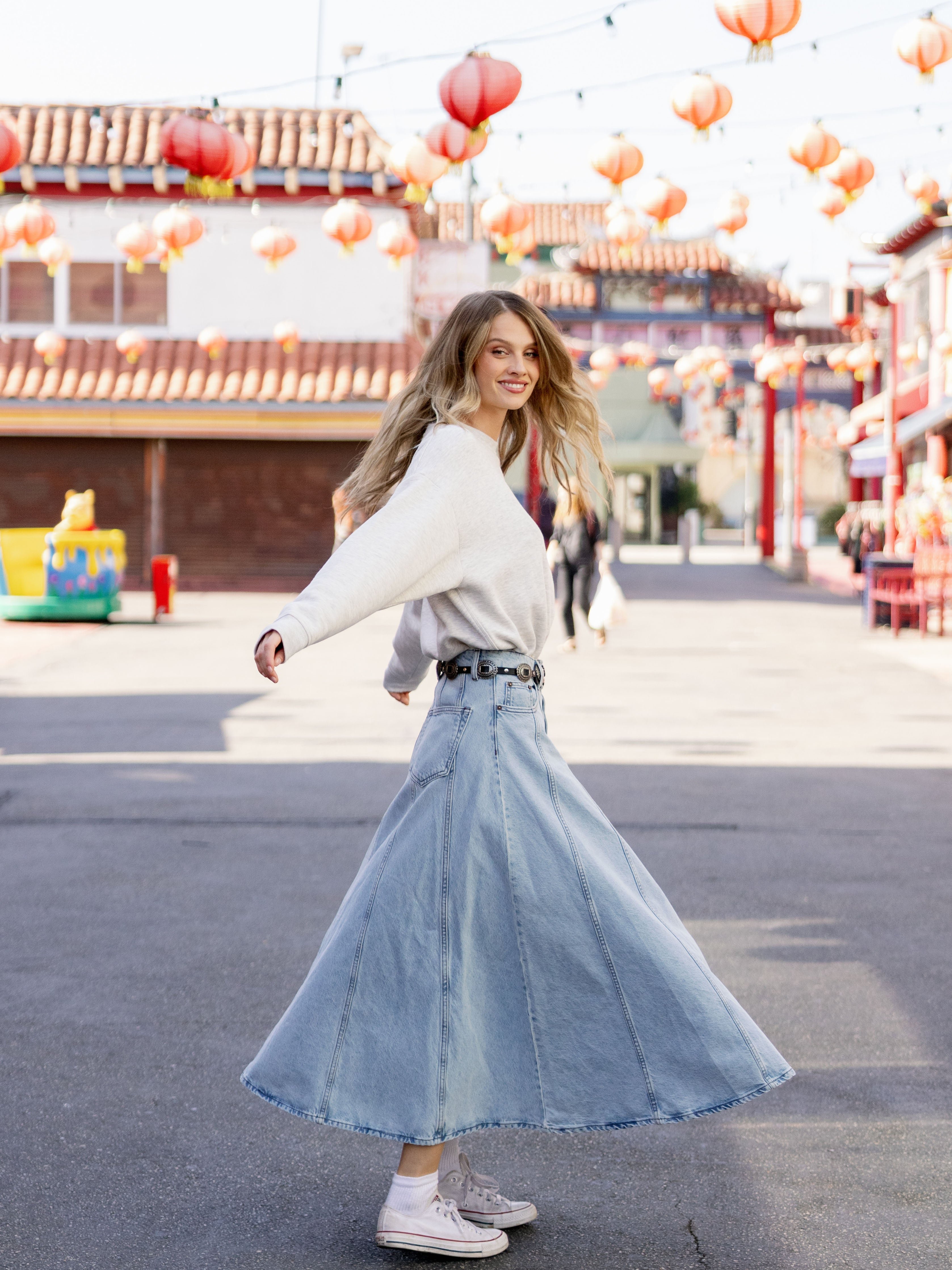 Heather Grey CityScape Pullover Crew. The Pullover is being worn by a female model. An accompanying jean skirt is being worn to complete the look of the outfit. The photo was taken with a downtown city background. 