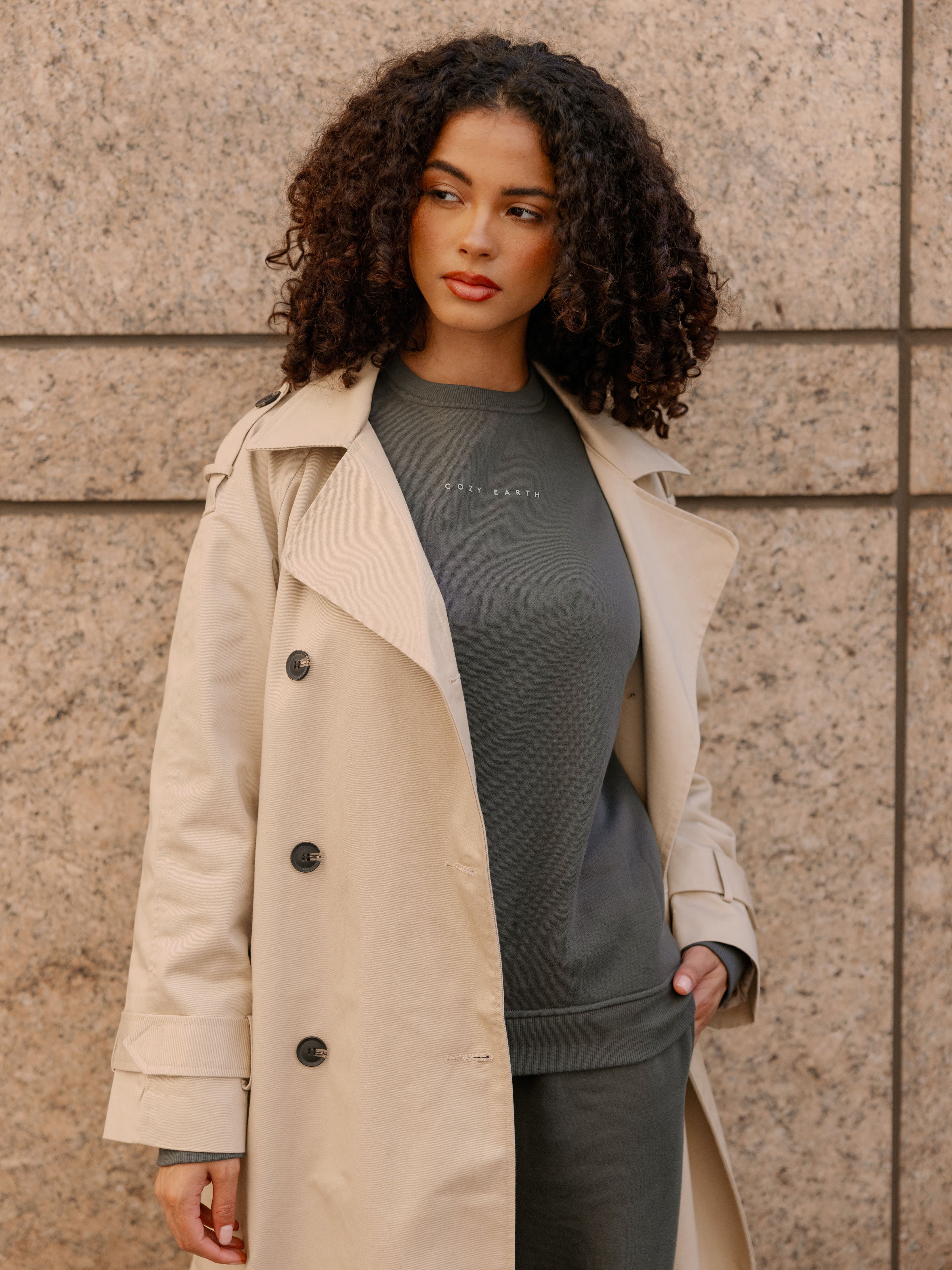 Storm CityScape Pullover Crew. The Pullover is being worn by a female model. Accompanying city scape clothing is being worn to complete the look of the outfit. The photo was taken with a city building background. 