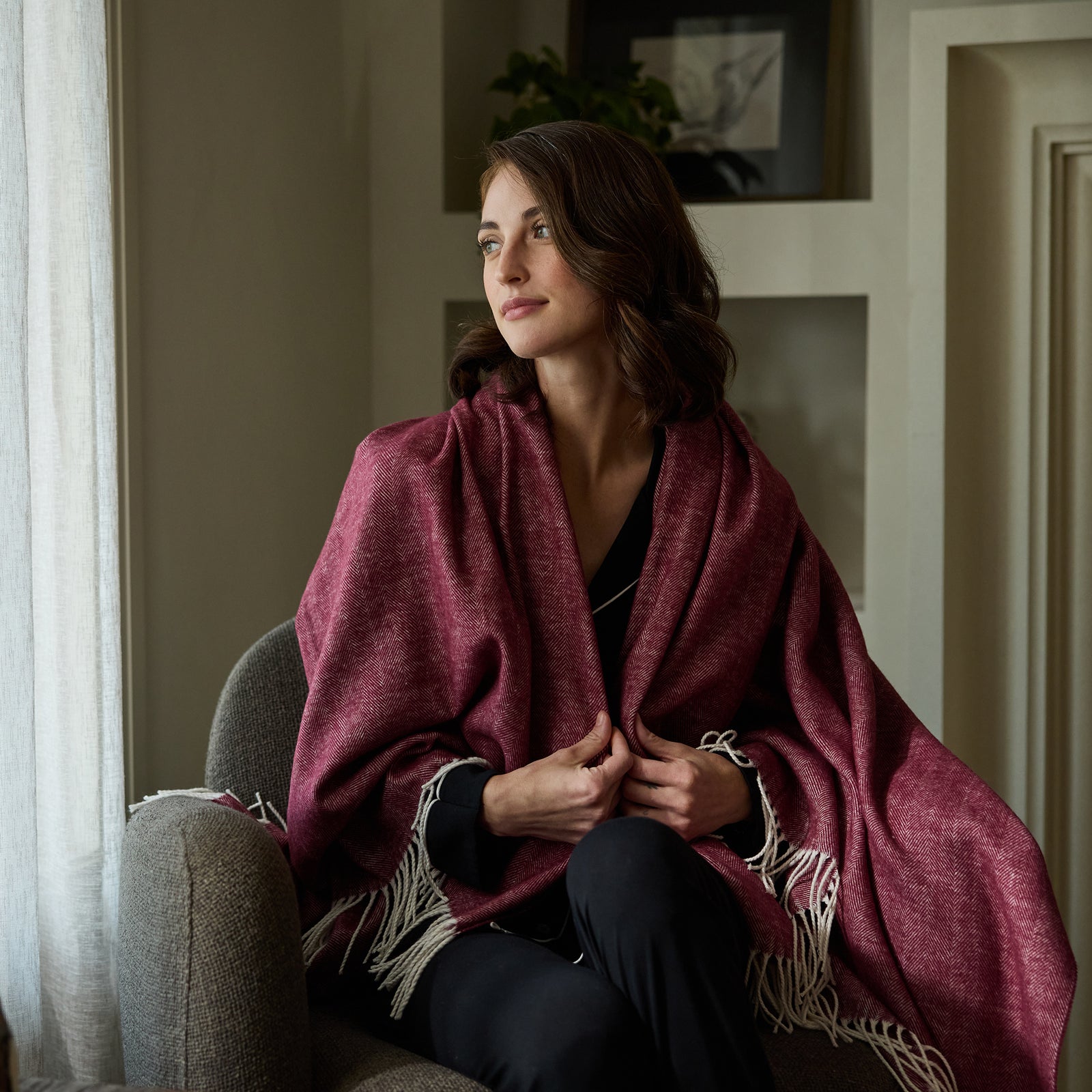 Woman sitting down with berry herringbone tassel throw wrapped around her 