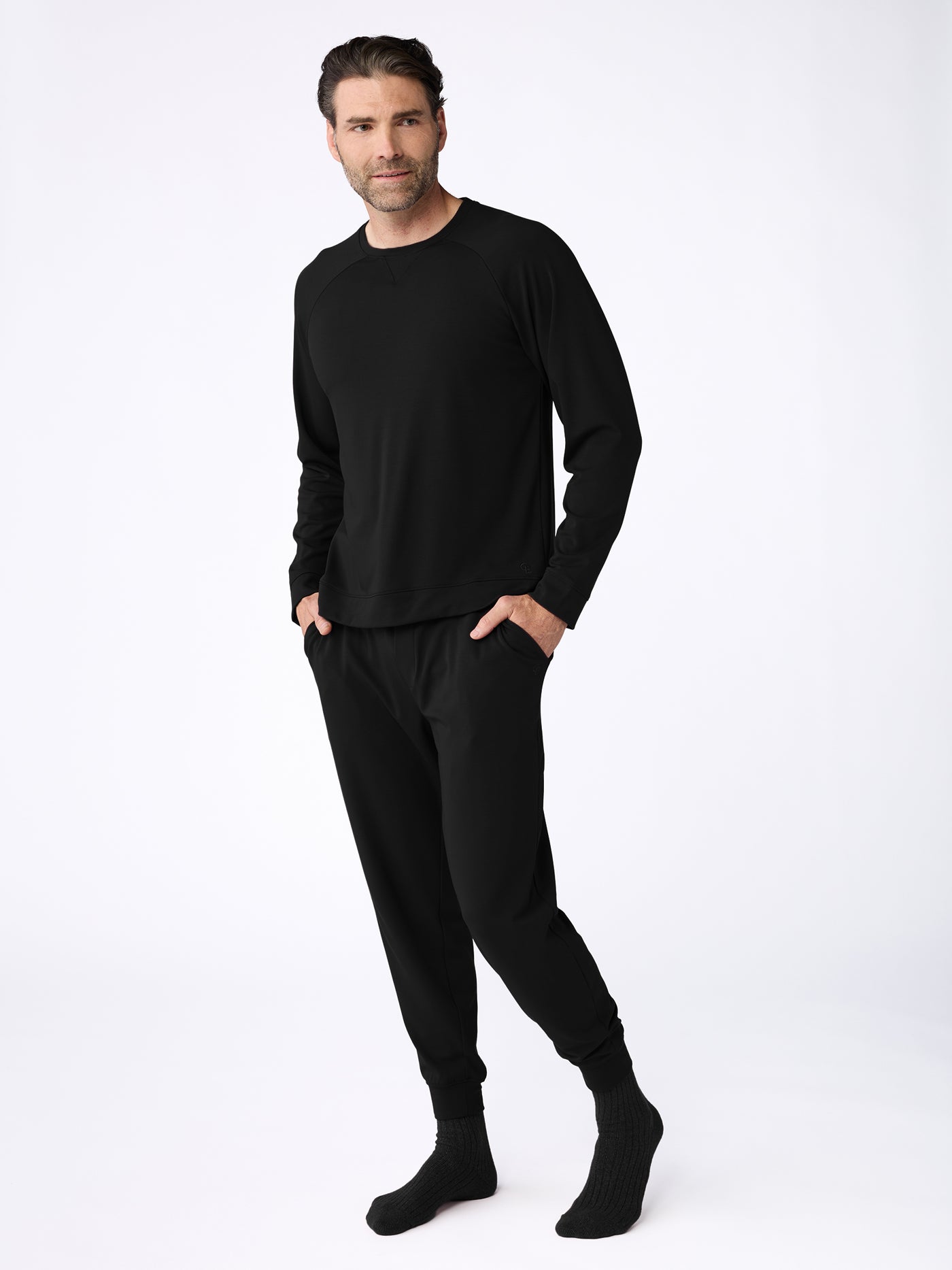 A man dons the Cozy Earth Men's Bamboo Jogger Set, with hands in pockets, pairing it perfectly with black socks against a plain white wall. 