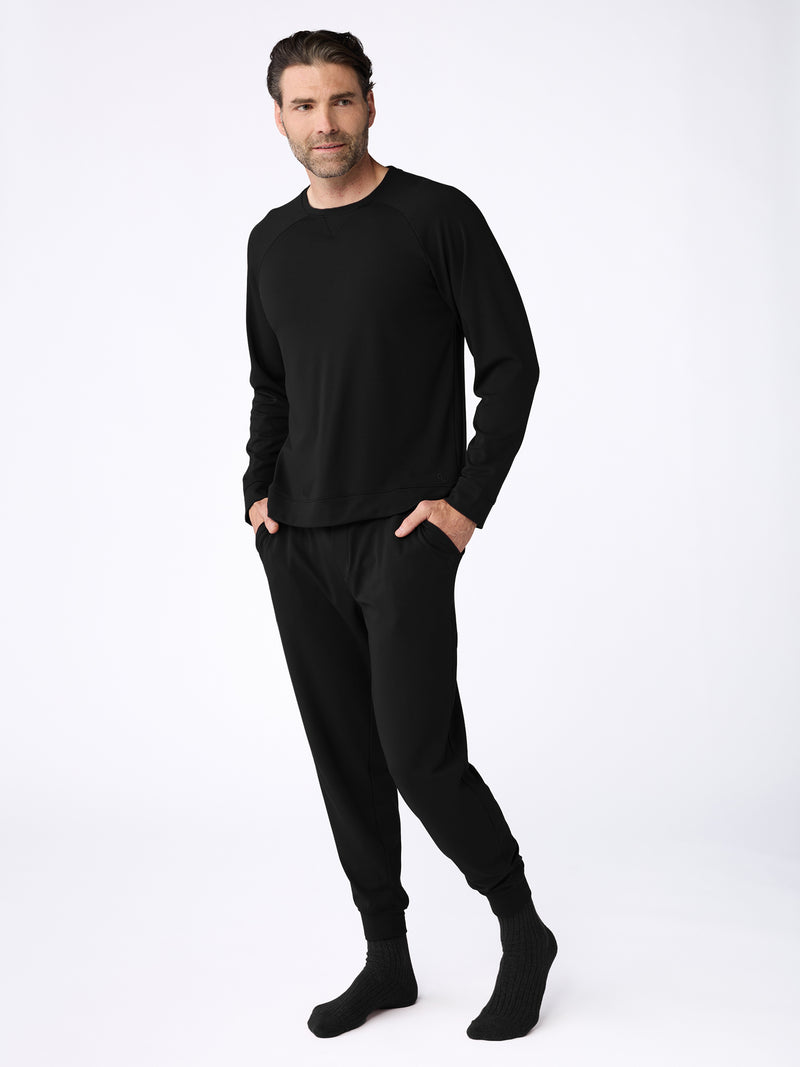 A man dons the Cozy Earth Men's Bamboo Jogger Set, with hands in pockets, pairing it perfectly with black socks against a plain white wall.