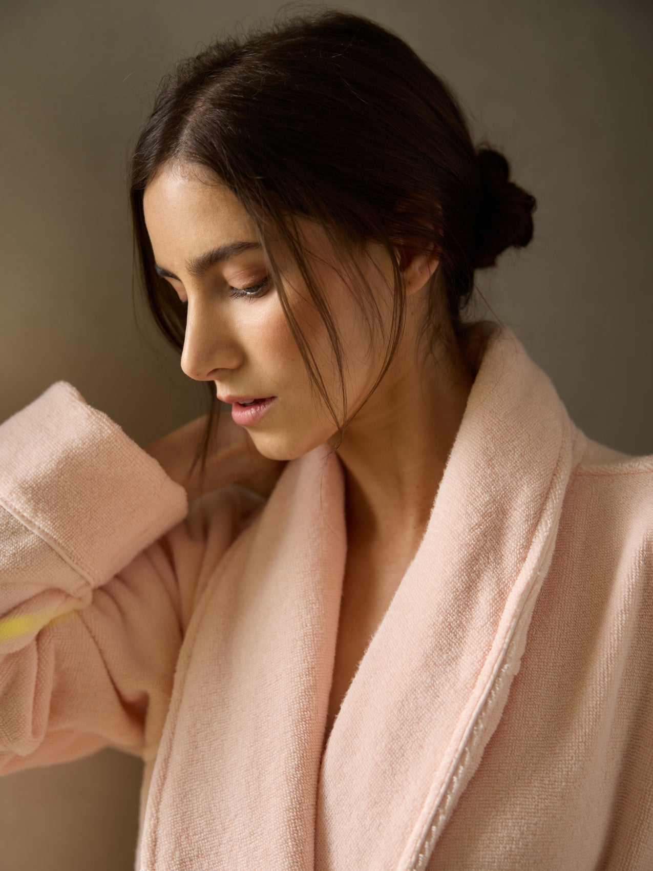 With dark hair in a bun and a serene expression, the person is wearing the Cozy Earth Luxe Bath Robe in soft pink, set against a neutral background. 