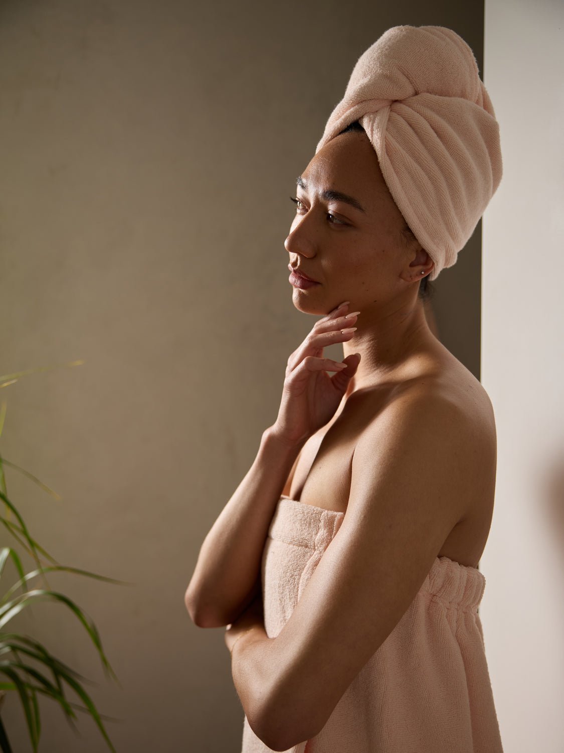 A woman stands in front of a neutral wall wearing a Cozy Earth Luxe Hair Towel and Wrap in Blossom. 