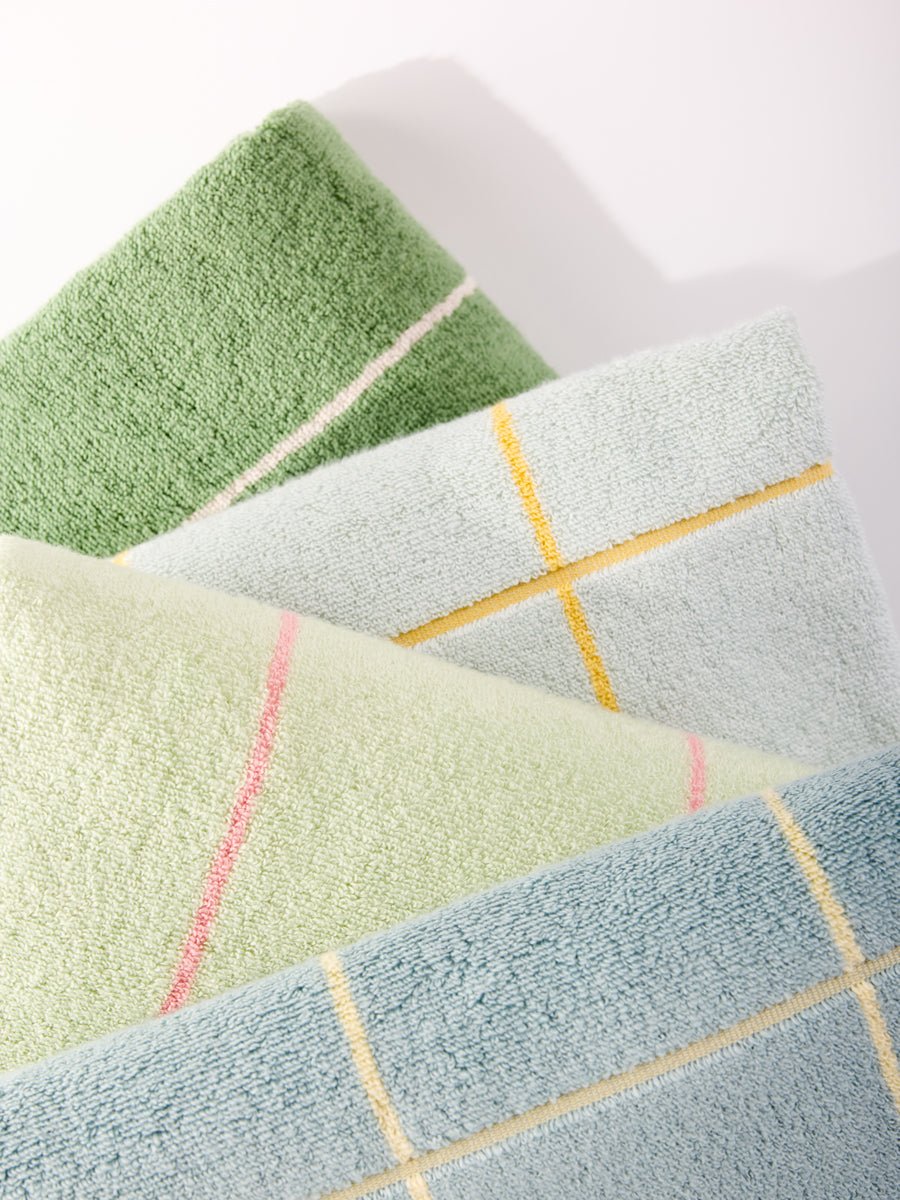 Close-up of Cozy Earth's Windowpane Resort Towels, folded in textured pastel shades like green, light green, and light blue with pink and yellow plaid patterns. The four towels are arranged overlapping on a white surface. 