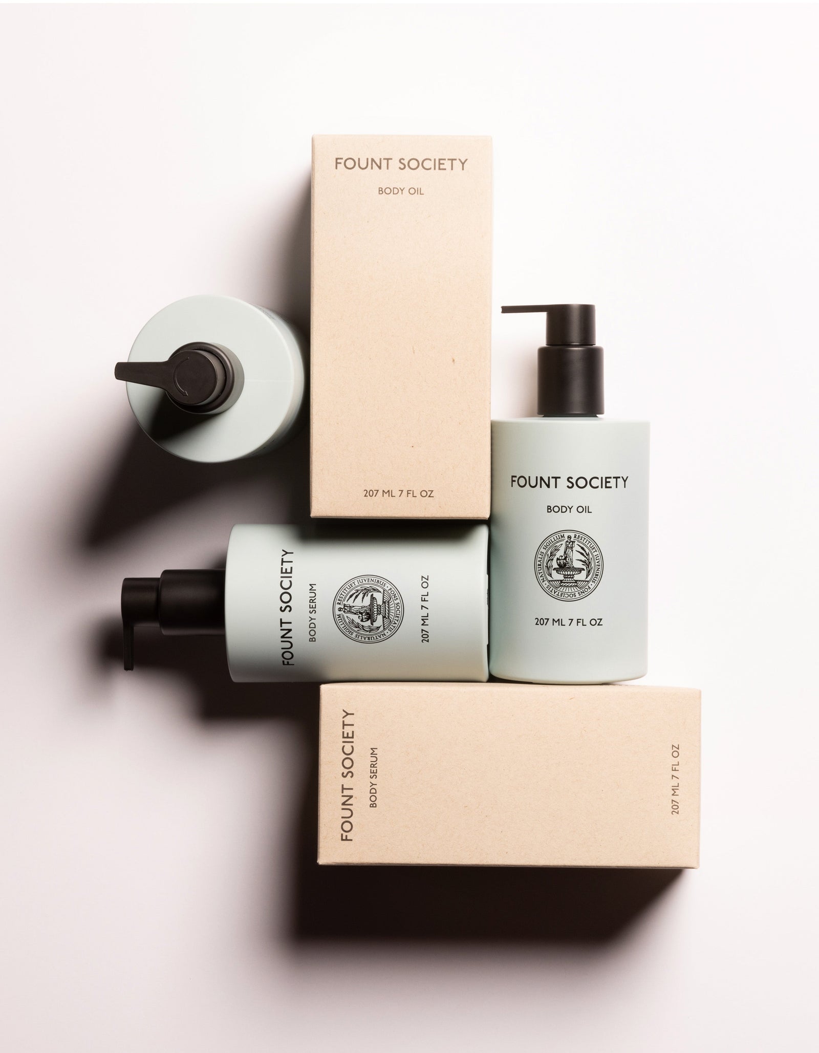 Three bottles of Cozy Earth's Body Glow Duo positioned alongside and on top of two cardboard boxes. The light green bottles have a black pump dispenser and feature a label with a circular emblem. The cardboard boxes are labeled "Body Glow Duo".