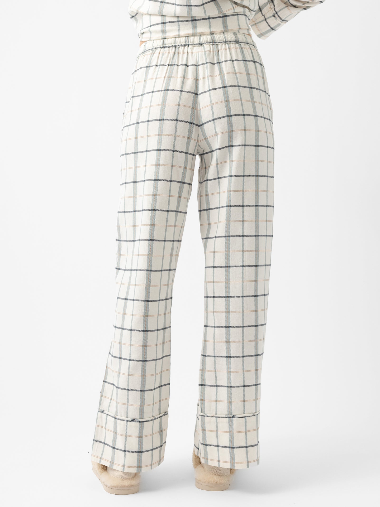 A person in a Women's Farmhouse Long Sleeve Pajama Set by Cozy Earth is shown from the waist down, wearing the white pants with a blue and grey checkered pattern. The pants have an elastic waistband and feature a relaxed fit with a slight flare at the bottom. 