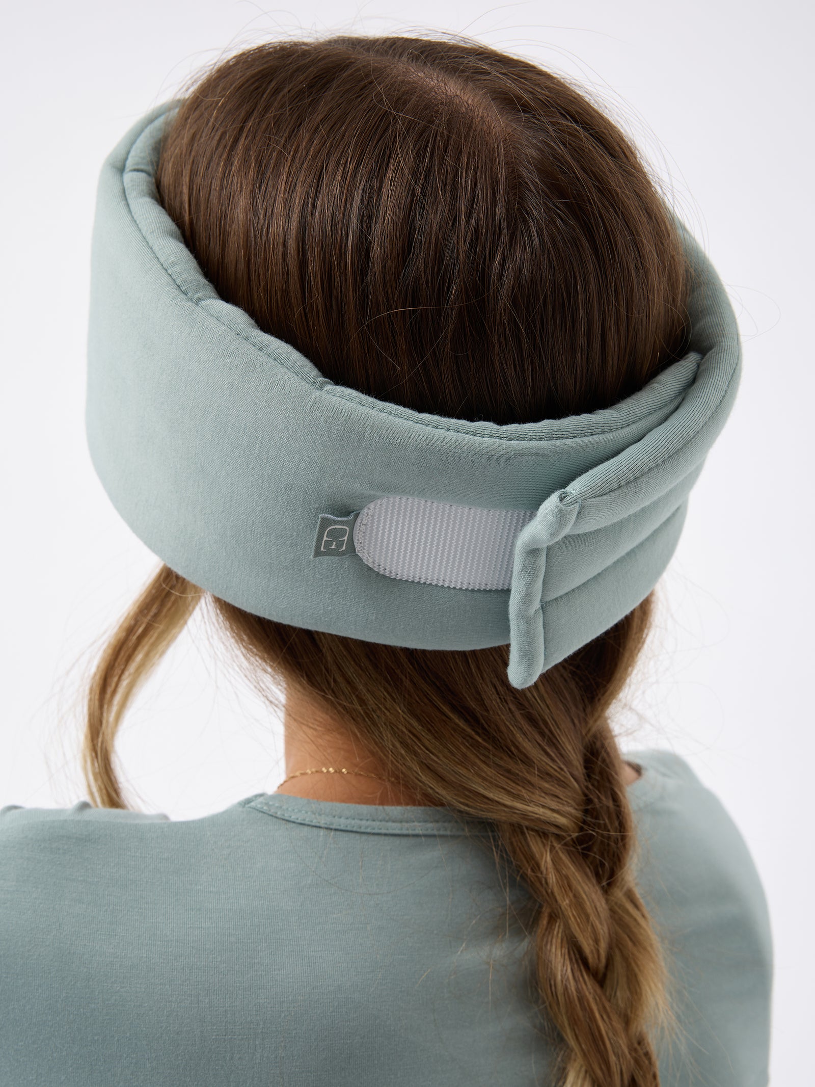 A woman wears the Cozy Earth Adjustable Bamboo Sleep Mask in Brook. She is facing away and showing where the mask fastens at the back. 