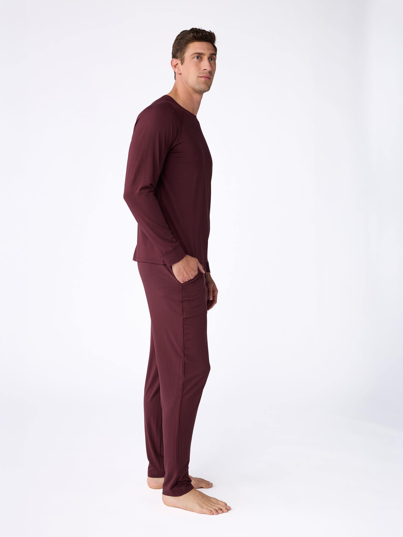 A man is barefoot against a simple background, wearing Cozy Earth's Stretch-Knit Bamboo Pajama Pant in maroon. He is facing sideways with his hands in his pockets. 