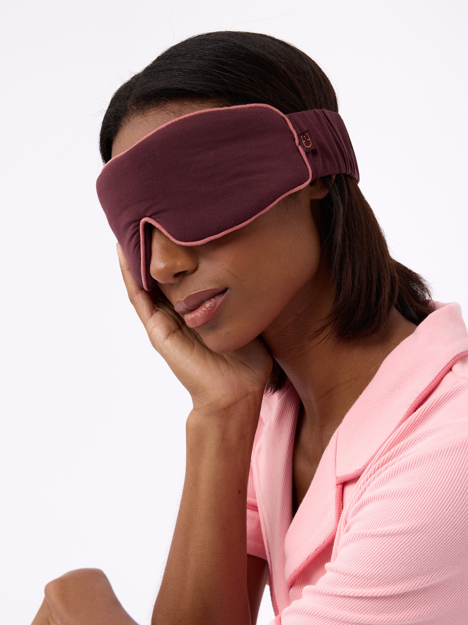 Woman wearing burgundy sleep mask with hand on her cheek 