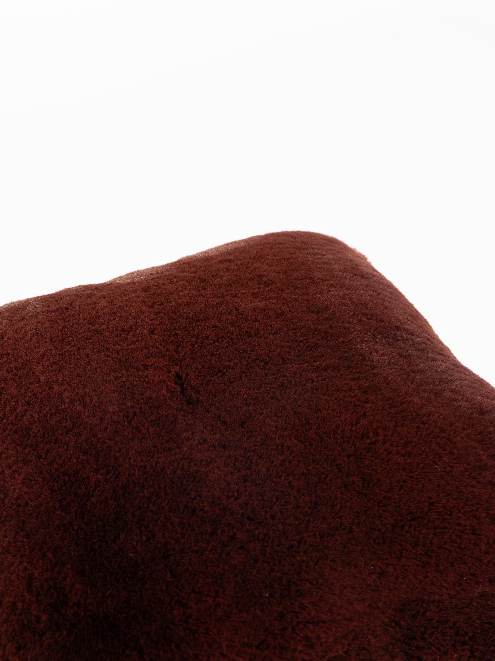 Close-up of a fluffy, dark brown Cuddle Pillow from Cozy Earth against a white background, highlighting its soft texture and smooth surface. 