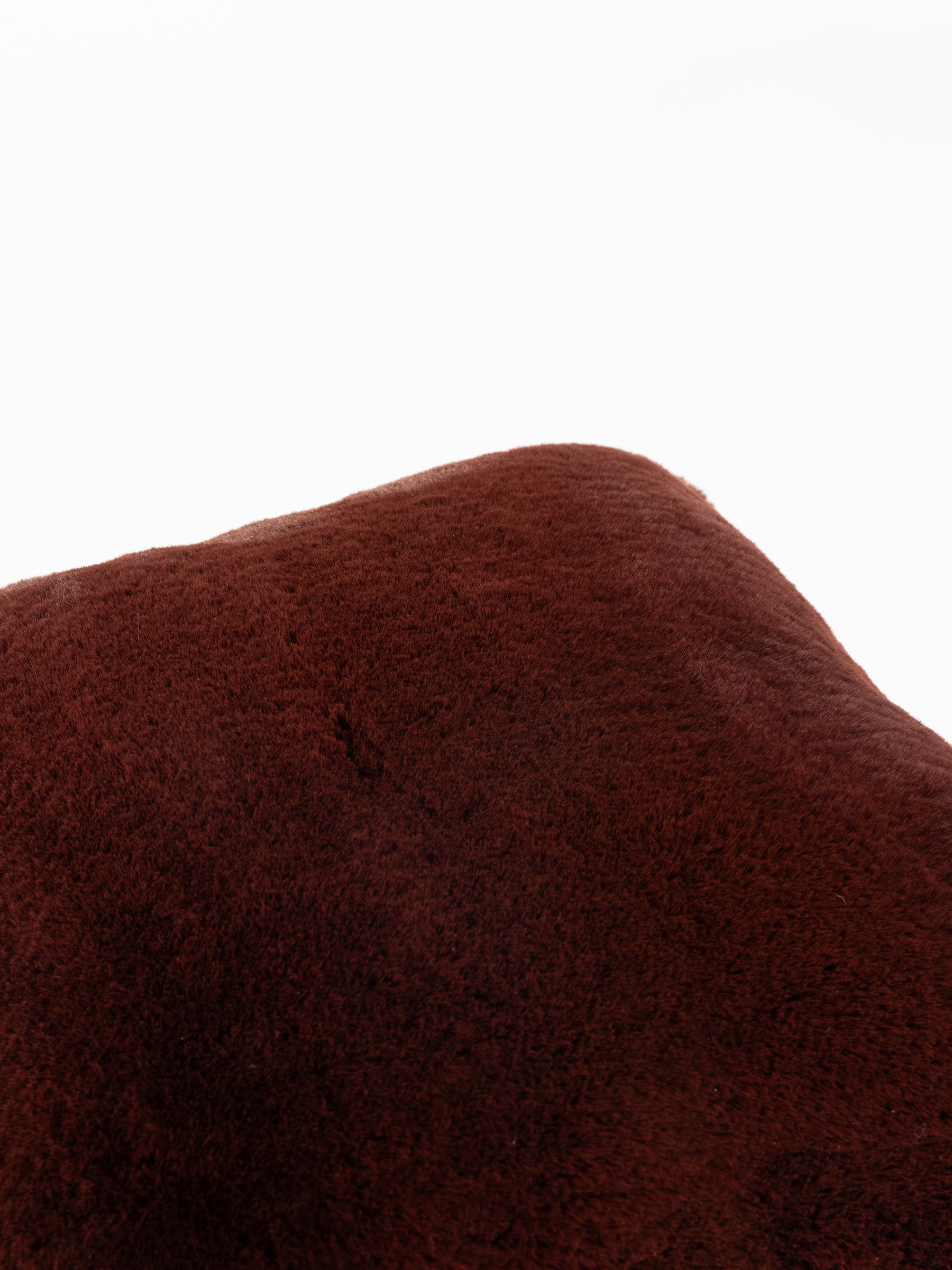 Close-up of a fluffy, dark brown Cuddle Pillow from Cozy Earth against a white background, highlighting its soft texture and smooth surface. |Color:Burgundy