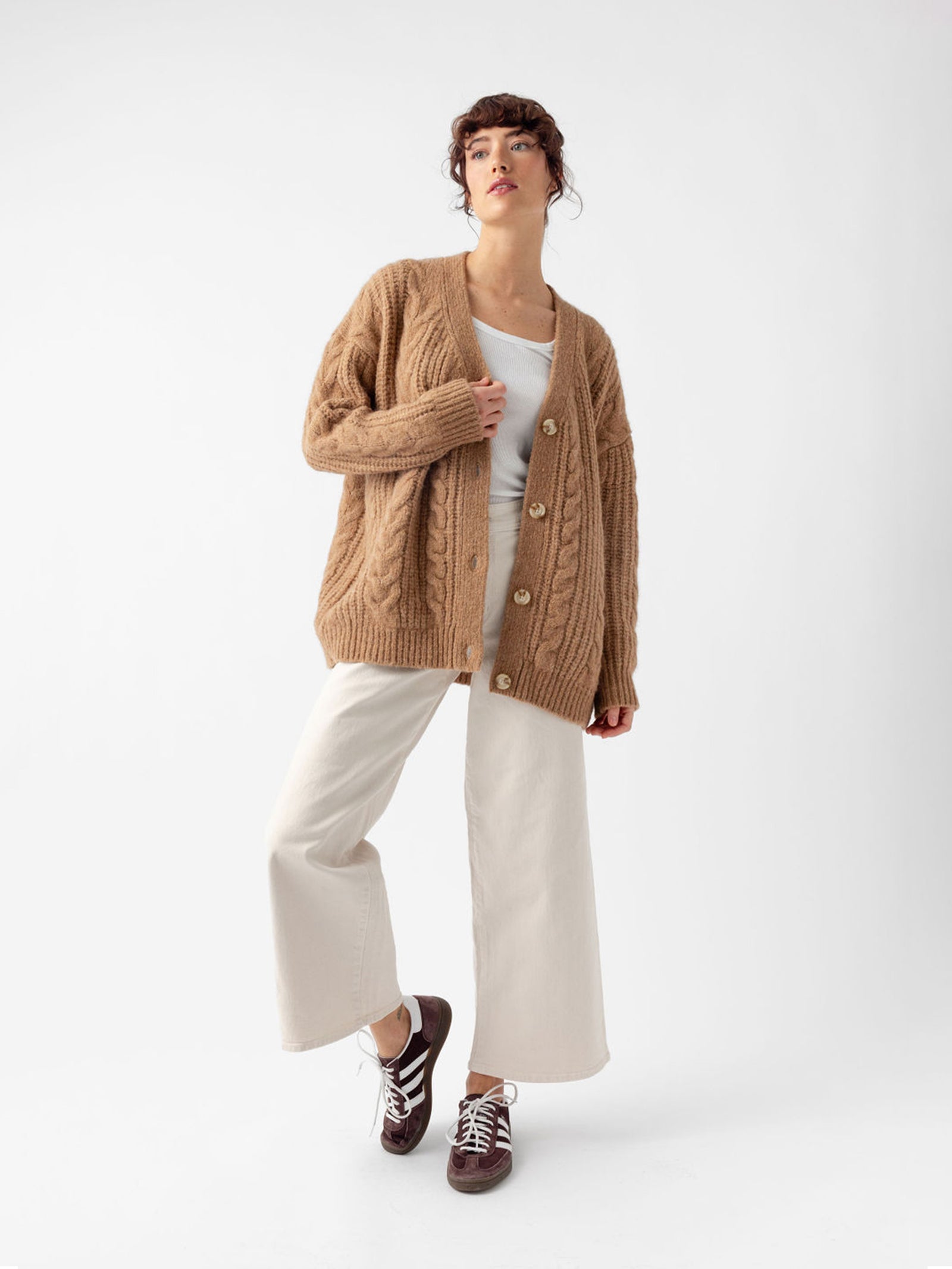 Studio image of woman in camel cardigan and off-white pants 