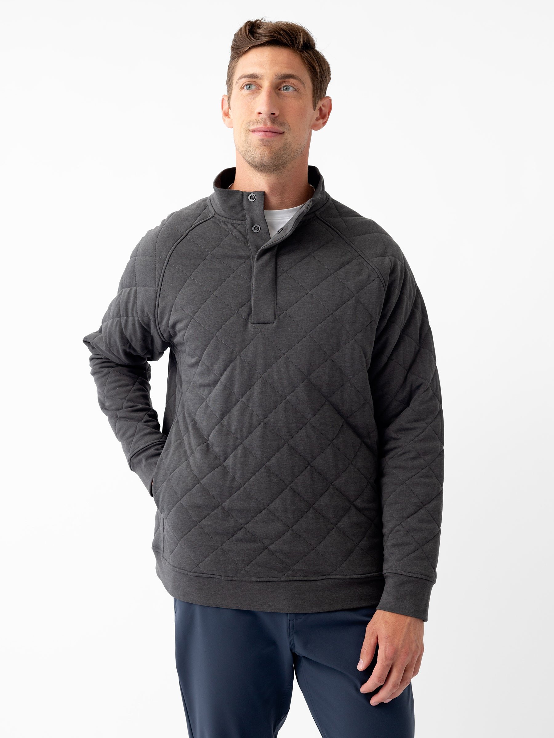 A person stands against a plain white background wearing a Cozy Earth Men's Ultra-Soft Bamboo Quilted Snap Pullover with a high collar and two buttons at the neckline. They have short hair and are looking slightly upward with a relaxed expression. Their hand rests casually in their pocket. |Color:Charcoal