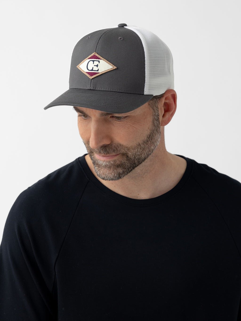 Man wearing charcoal/white diamond mesh trucker hat looking down 