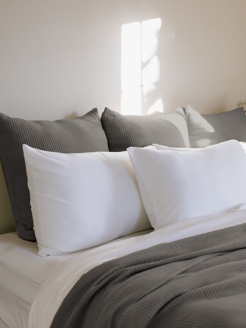 Charcoal euro coverlet shams behind white pillows on a bed