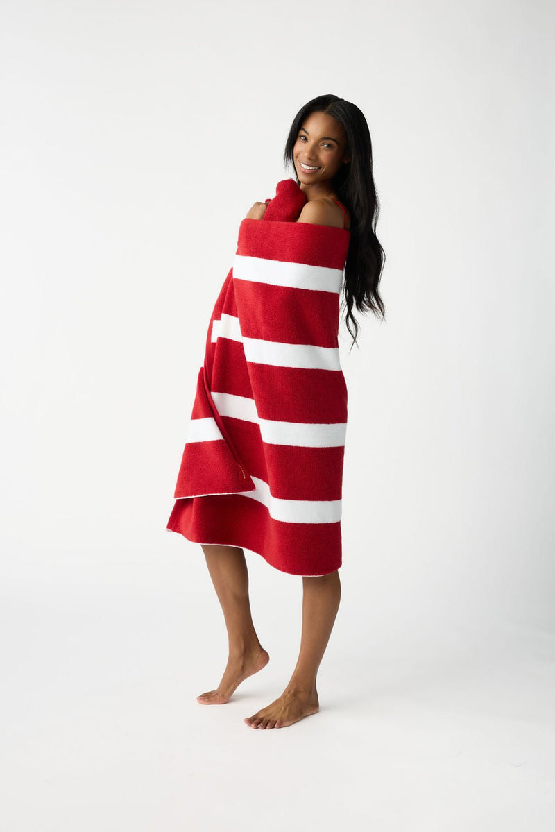 A person smiles while wrapped in a Cozy Earth Classic Stripe Resort Towel, standing barefoot against a plain white background.