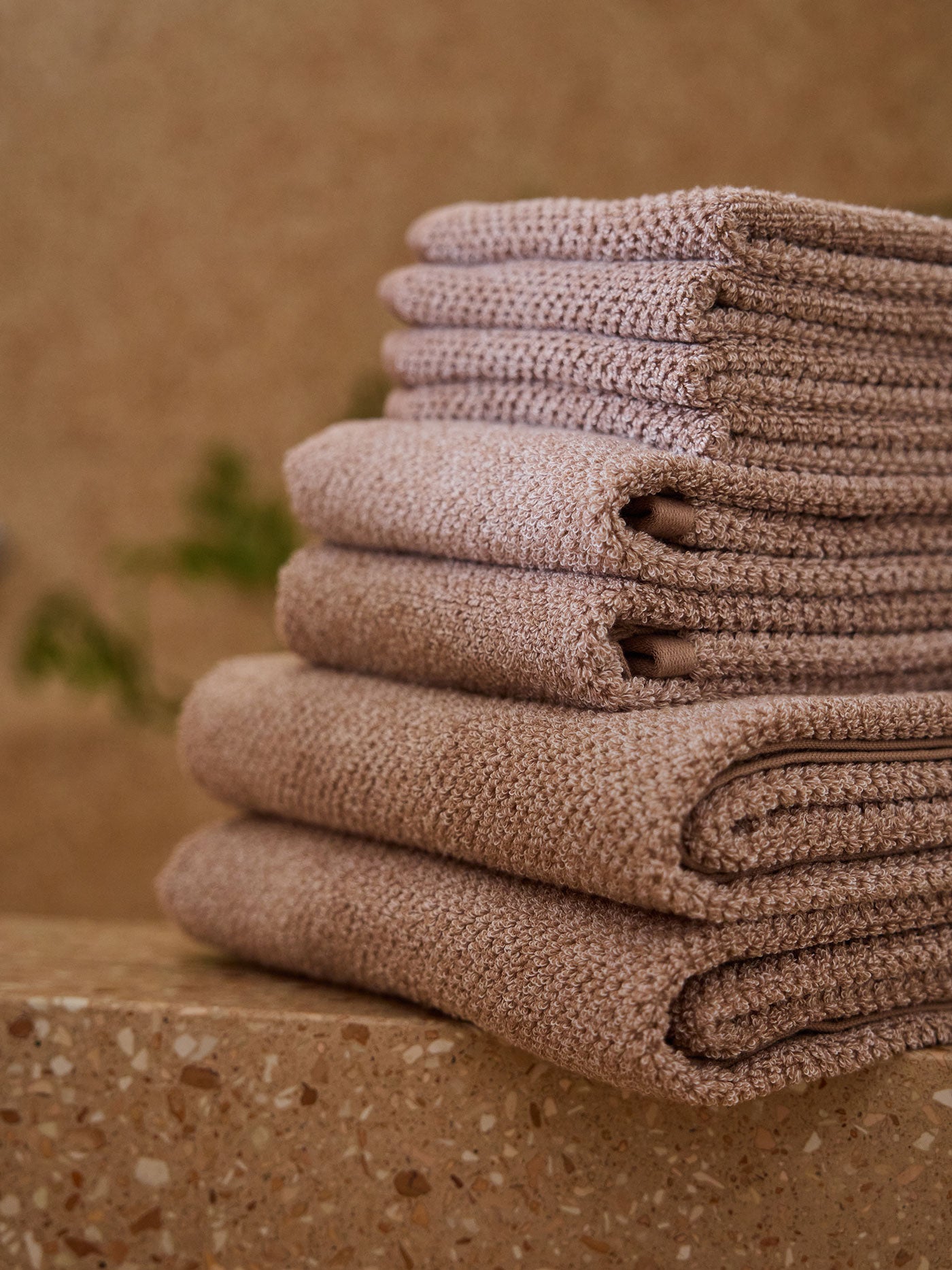 A stack of Cozy Earth bath towels sit on the edge of a stone bathtub. 