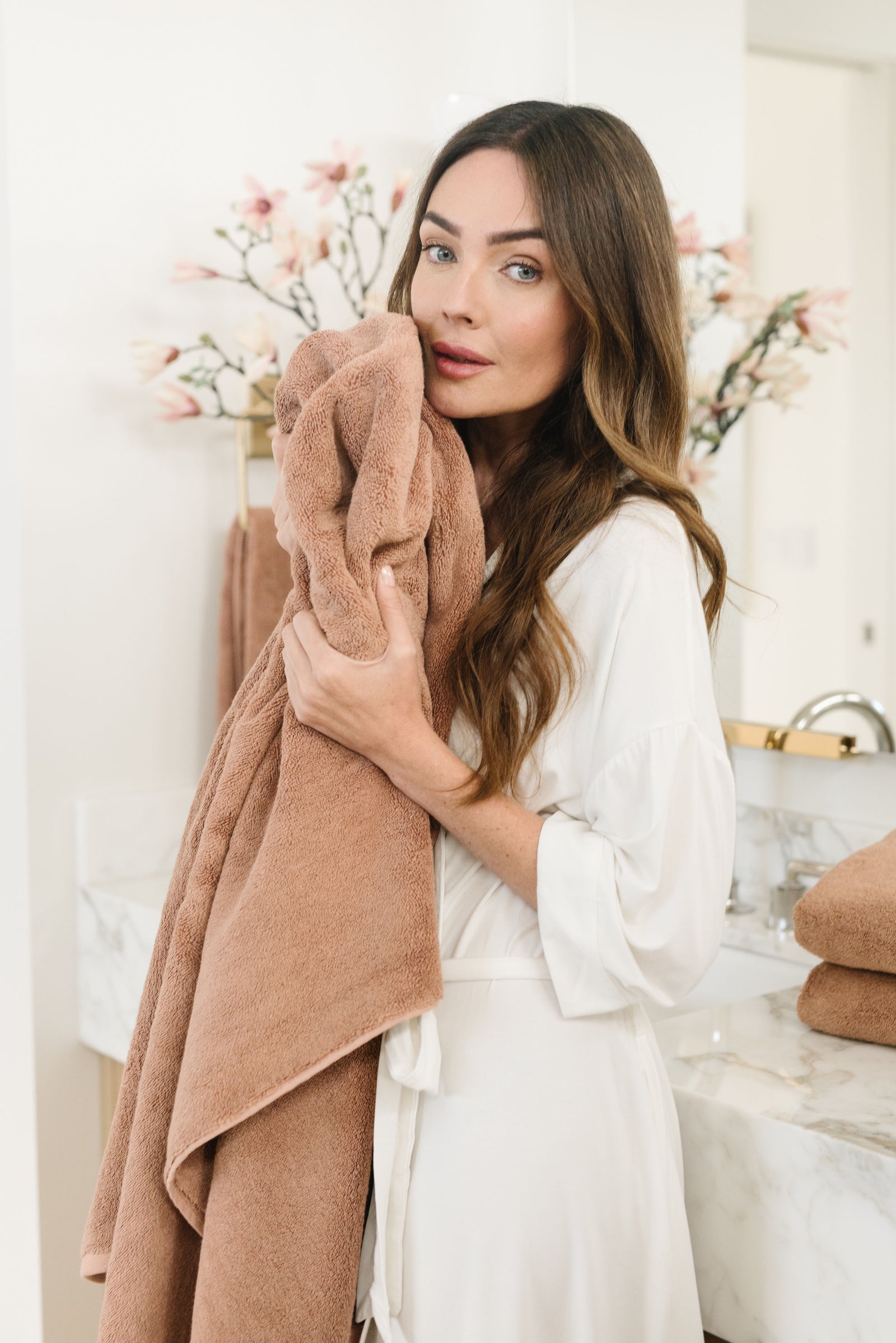 Premium Plush Bath Towel in the color Clay. Photo of Clay Premium Plush Bath Towel taken with a brunette woman holding the towel close to her body in a bathroom. 