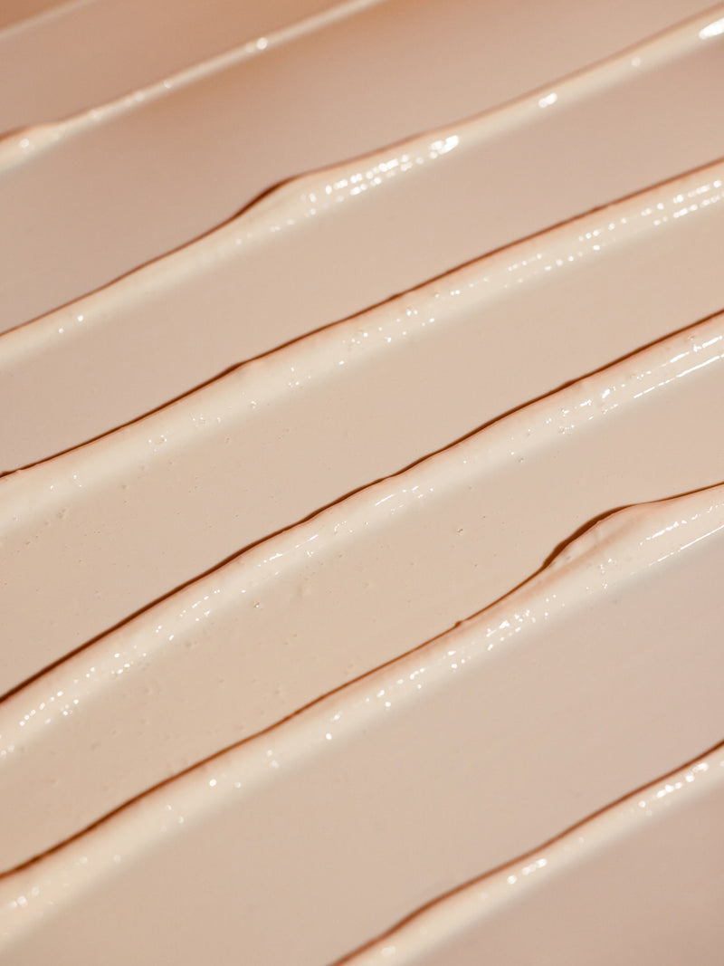 A close-up of the creamy, smooth lines of Cozy Earth's Clay Mask showcases a textured beige pattern on the surface. The light highlights intricate ridges and valleys, adding depth and richness to its appearance.