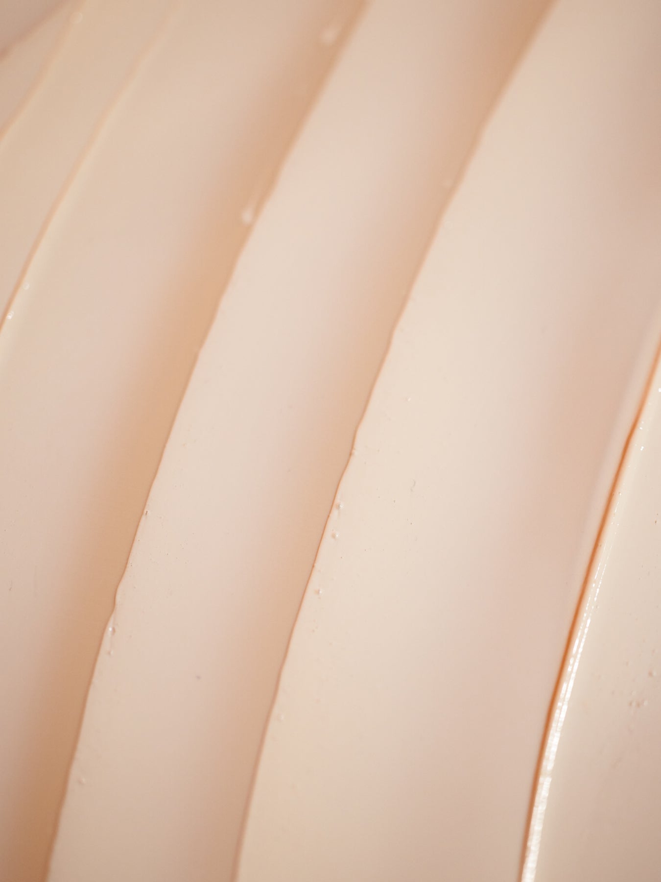 A close-up of the smooth, cream-colored surface of Cozy Earth's Clay Mask. Gentle lighting highlights its texture, showing parallel lines and a glossy appearance. 