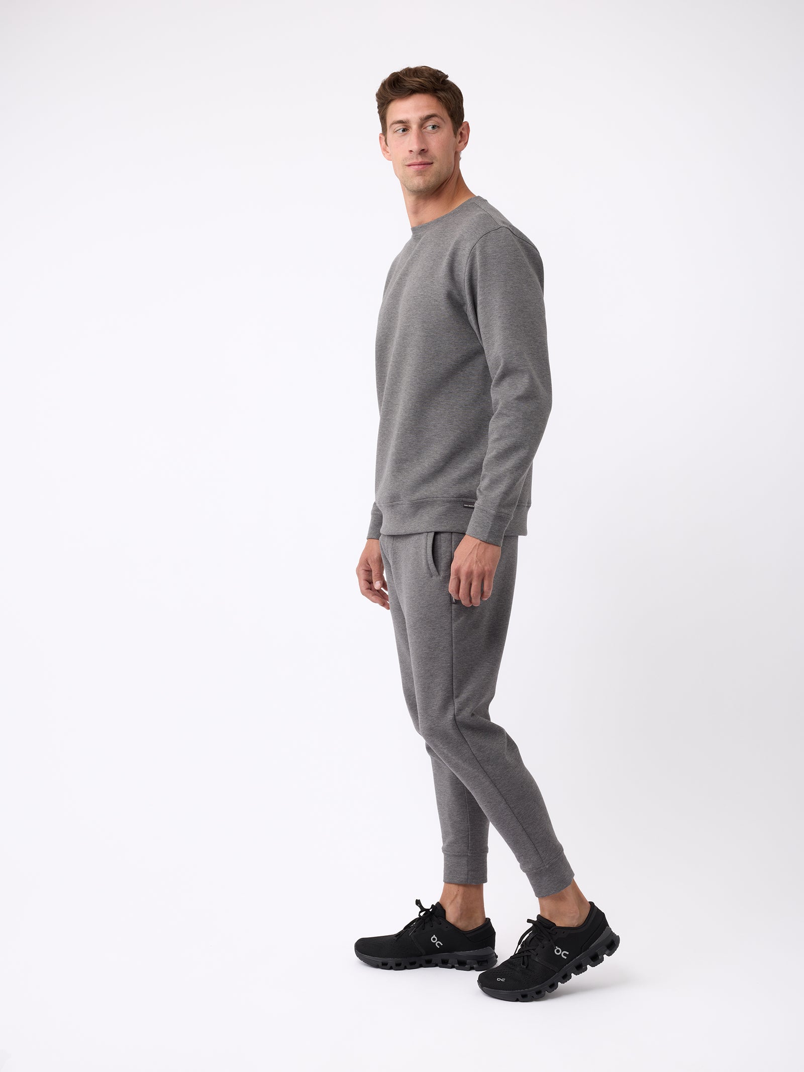 A man wearing the Cozy Earth Men's StretchTech Jogger and black sneakers stands against a plain white background, looking slightly to the side. 