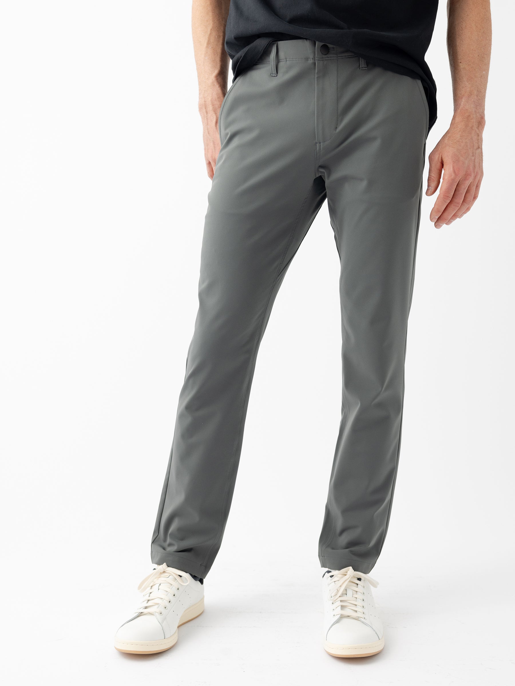 A person is standing against a plain white background wearing the Men's Everywhere Pant 30L by Cozy Earth in gray, paired with white sneakers. The person's upper body is partially visible, showing just the lower part of a black shirt and one arm hanging down. |Color:Coal