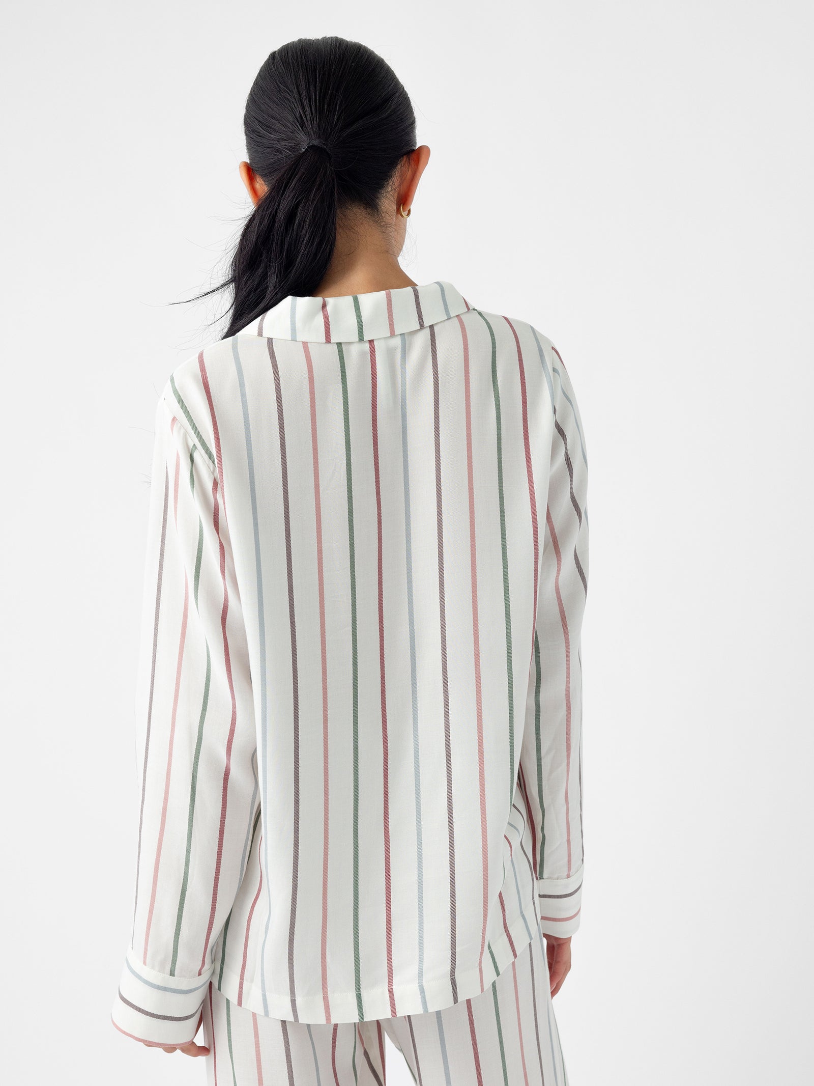 A person with long black hair is facing away, wearing the Women's Soft Woven Long Sleeve Pajama Top by Cozy Earth, which features light-colored fabric adorned with vertical red, green, and gray stripes. The background is plain white. 