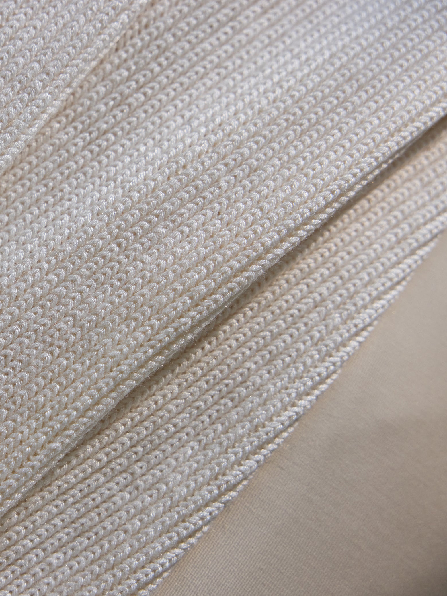 Close up of creme Classic Knit Blanket draped over a bed. 