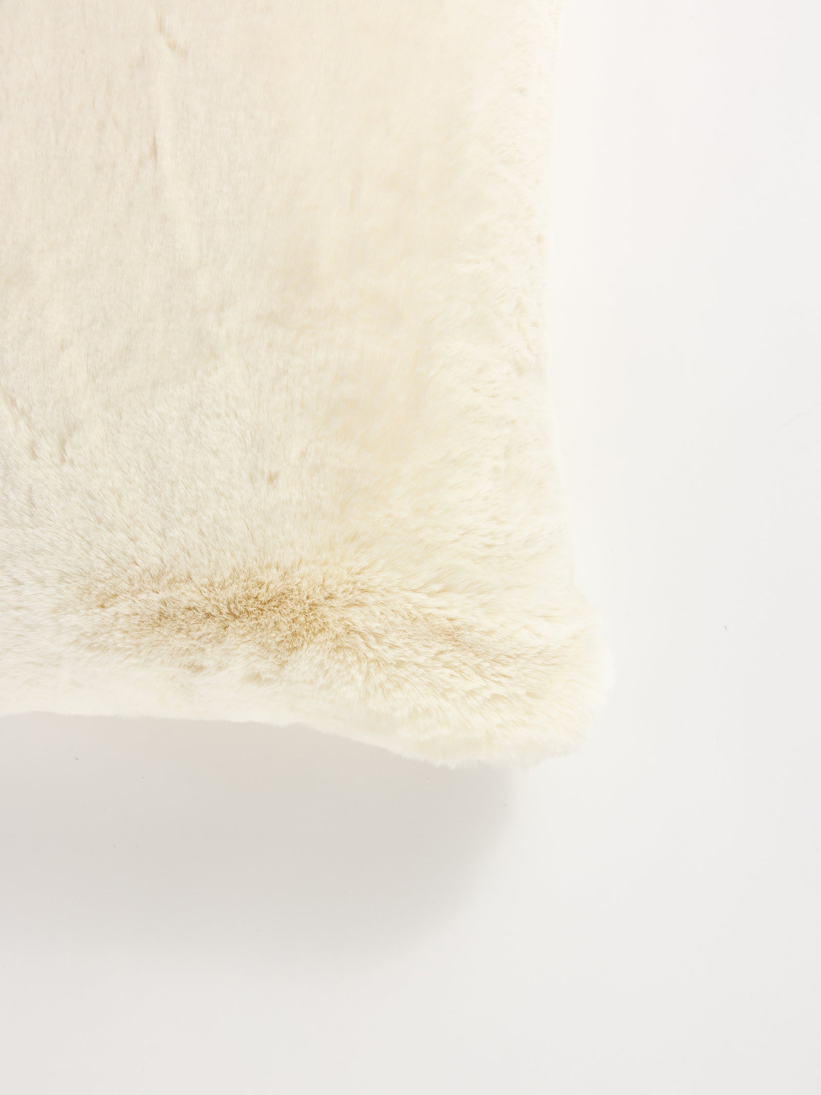 A close-up of the Cuddle Pillow by Cozy Earth showcases its soft, creamy white faux fur texture. The plush surface looks smooth and cozy, with subtle shading variations for a realistic touch. Gentle lighting highlights a corner of the fabric in this image. 