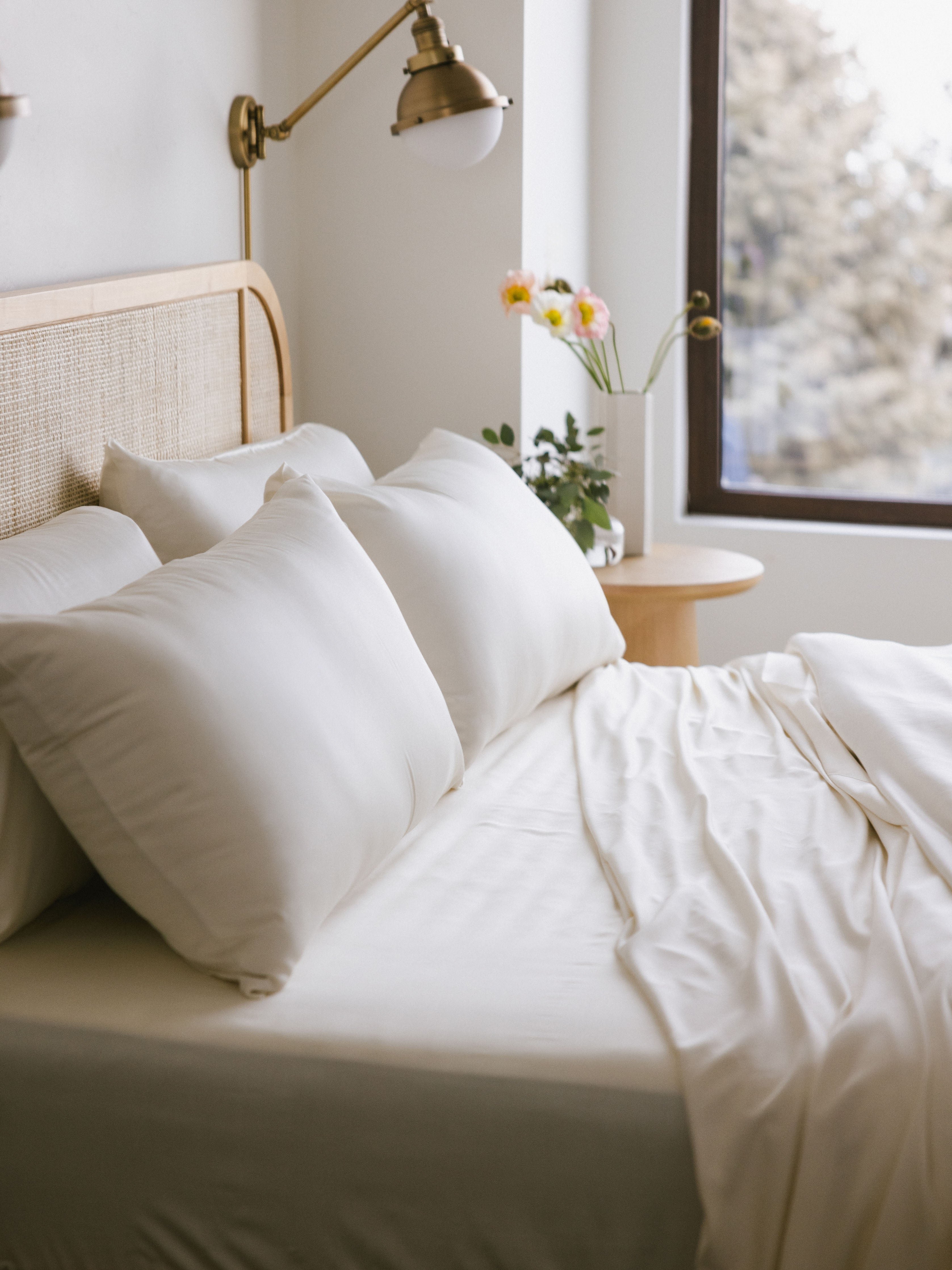 Unmade bed with creme bedding showing four pillows close up 