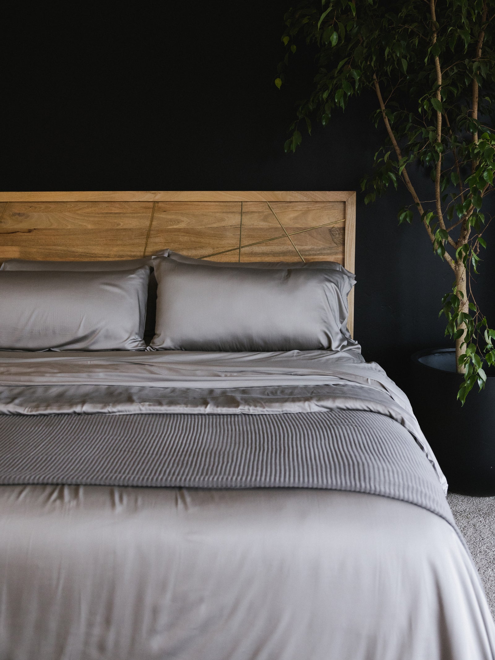 Bed made with dove grey sheets and a wooden headboard 