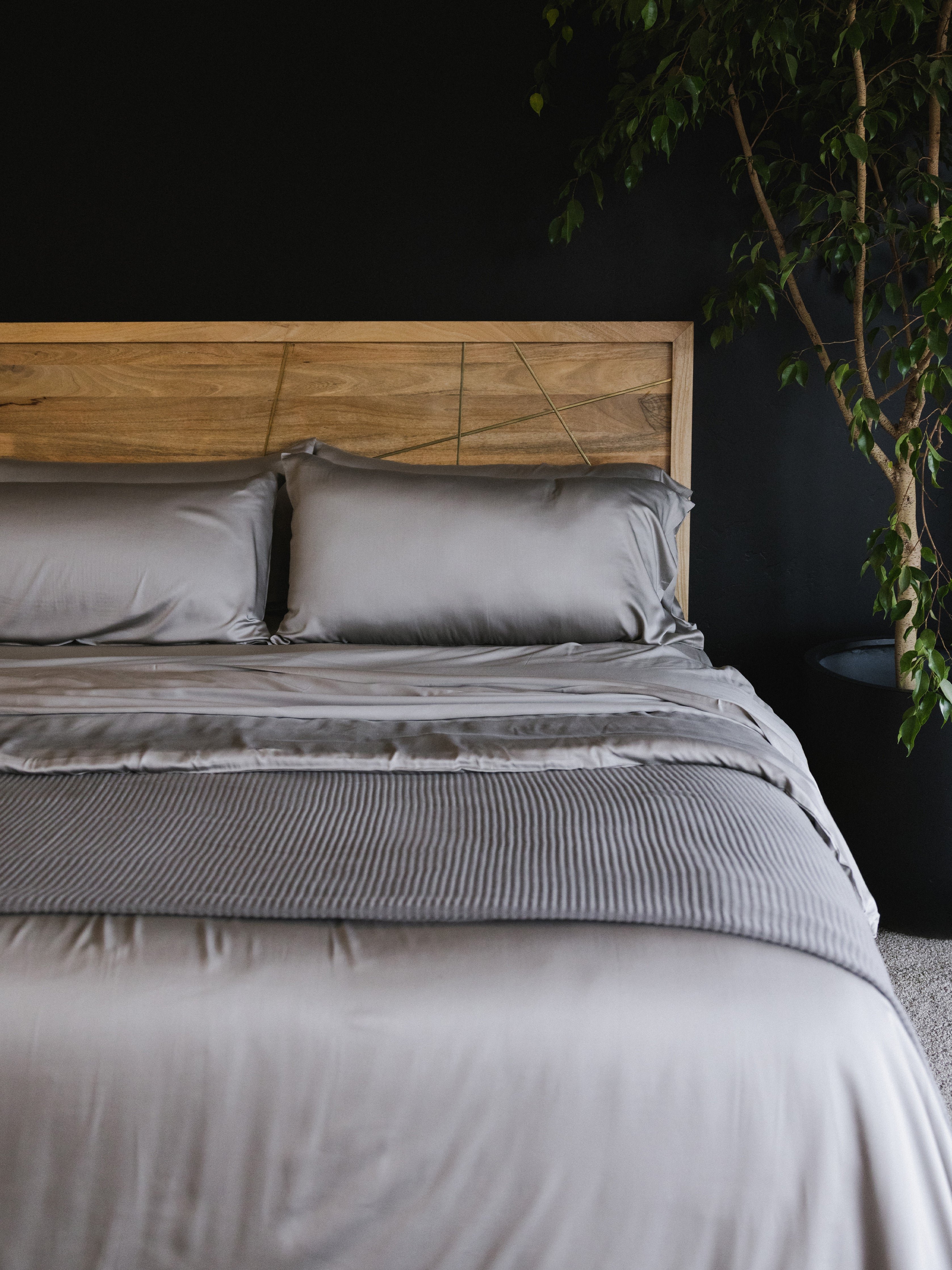 Bed made with dove grey sheets and a wooden headboard 