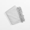 A folded Bamboo Tassel Throw from Cozy Earth, in a light gray color, lies on a white background. The throw appears soft and plush, with wavy and textured fringes that add a decorative touch to its otherwise simple design. |Color:Dove Grey