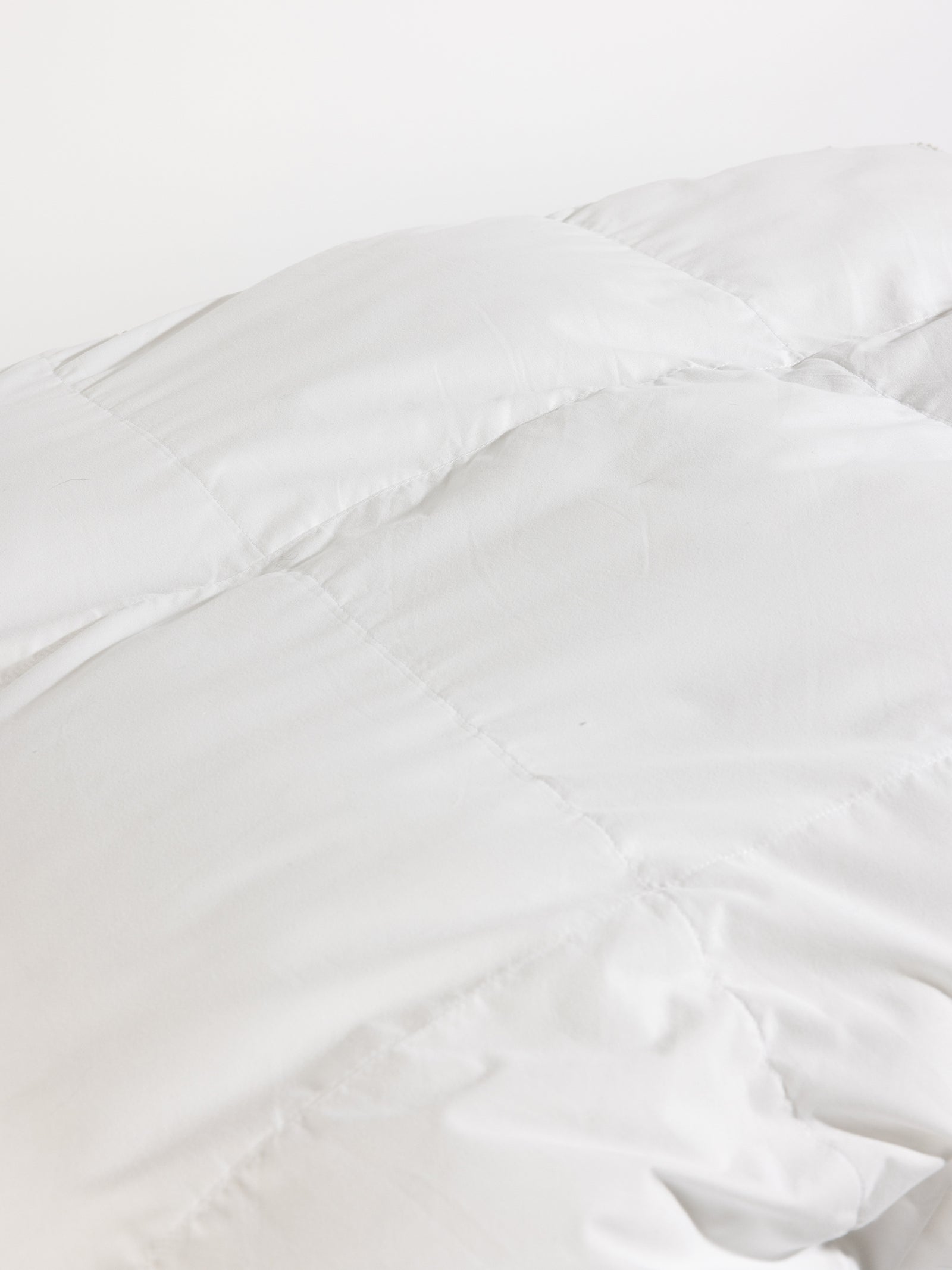 Close-up of a white, quilted fabric with visible stitching, creating a checkerboard pattern. The material appears soft and plush, suggesting it is part of the Cozy Earth's Down Alternative Comforter.