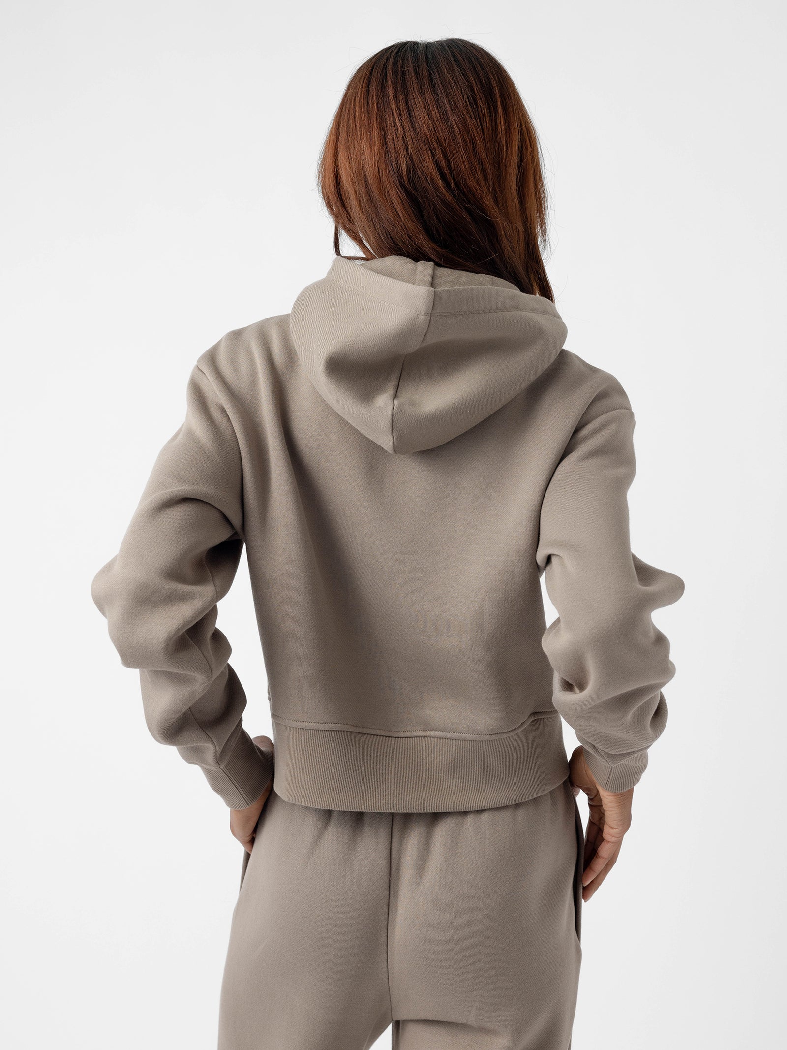 A person with long hair is shown from the back, wearing a light gray Women's CityScape Cropped Hoodie and matching sweatpants by Cozy Earth. The hoodie has a relaxed and casual style. The background is plain white. 