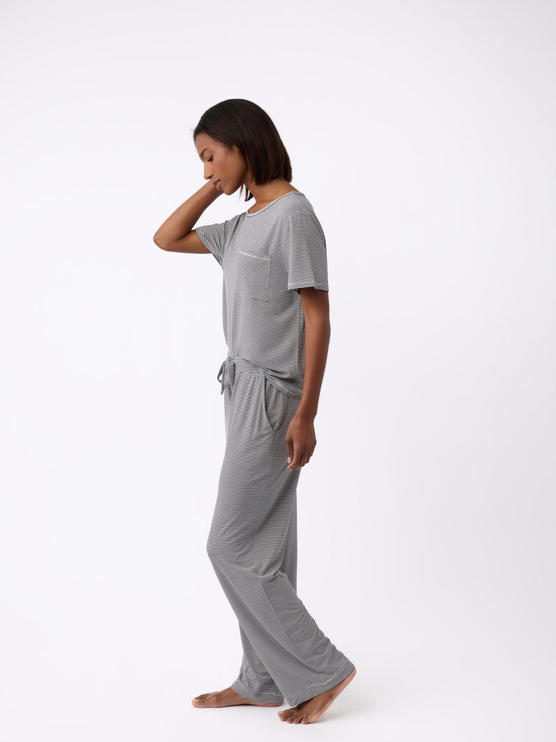 Against a white backdrop, someone is barefoot, wearing the Cozy Earth Women’s Bamboo Stretch-Knit Pant in gray. The wide-leg pants and matching short-sleeve top offer a relaxed fit with a tied waist.