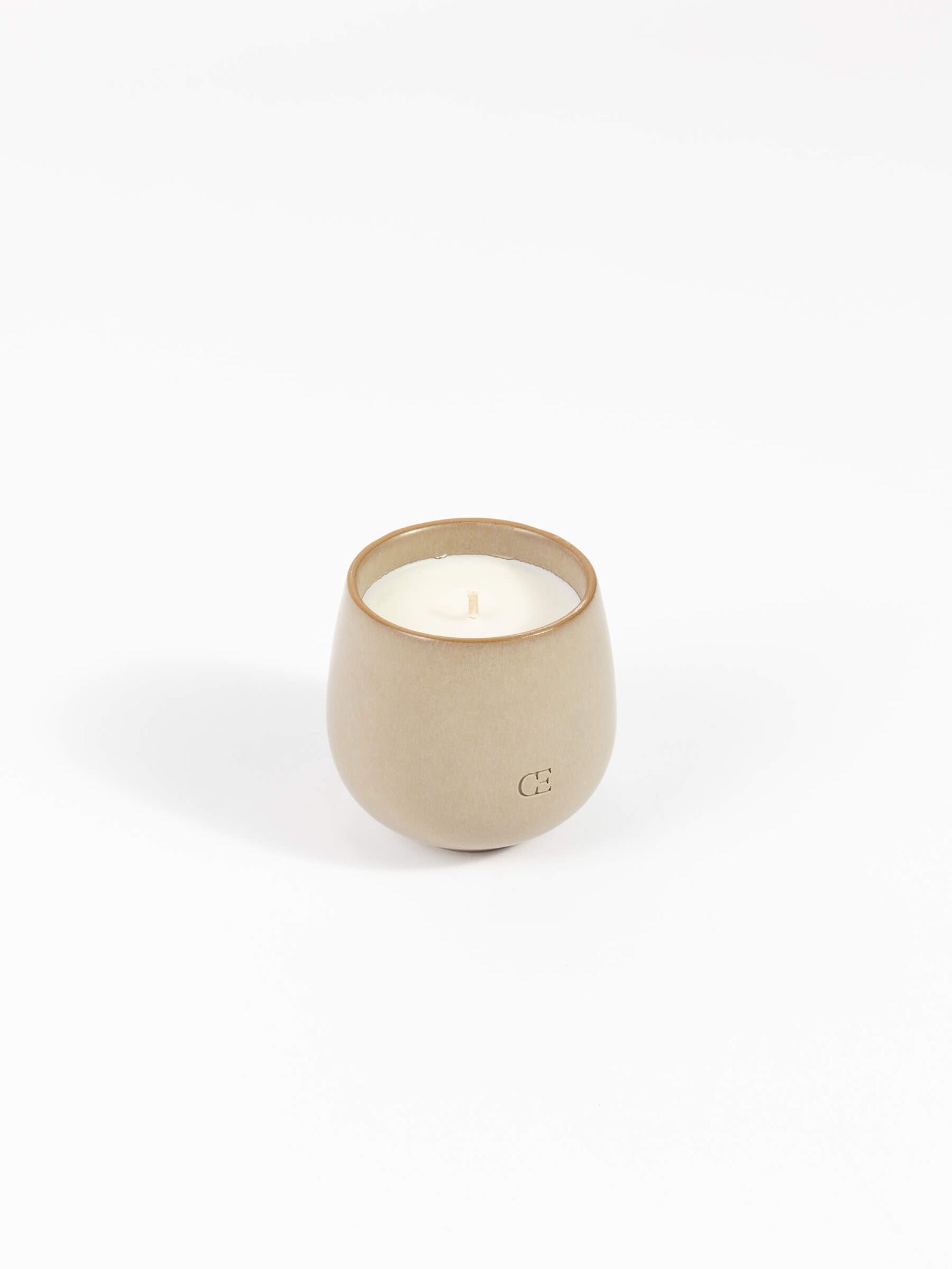 The Candle EMBER by Cozy Earth is a small, round, beige ceramic holder filled with white wax and an unlit wick, displayed on a white background.