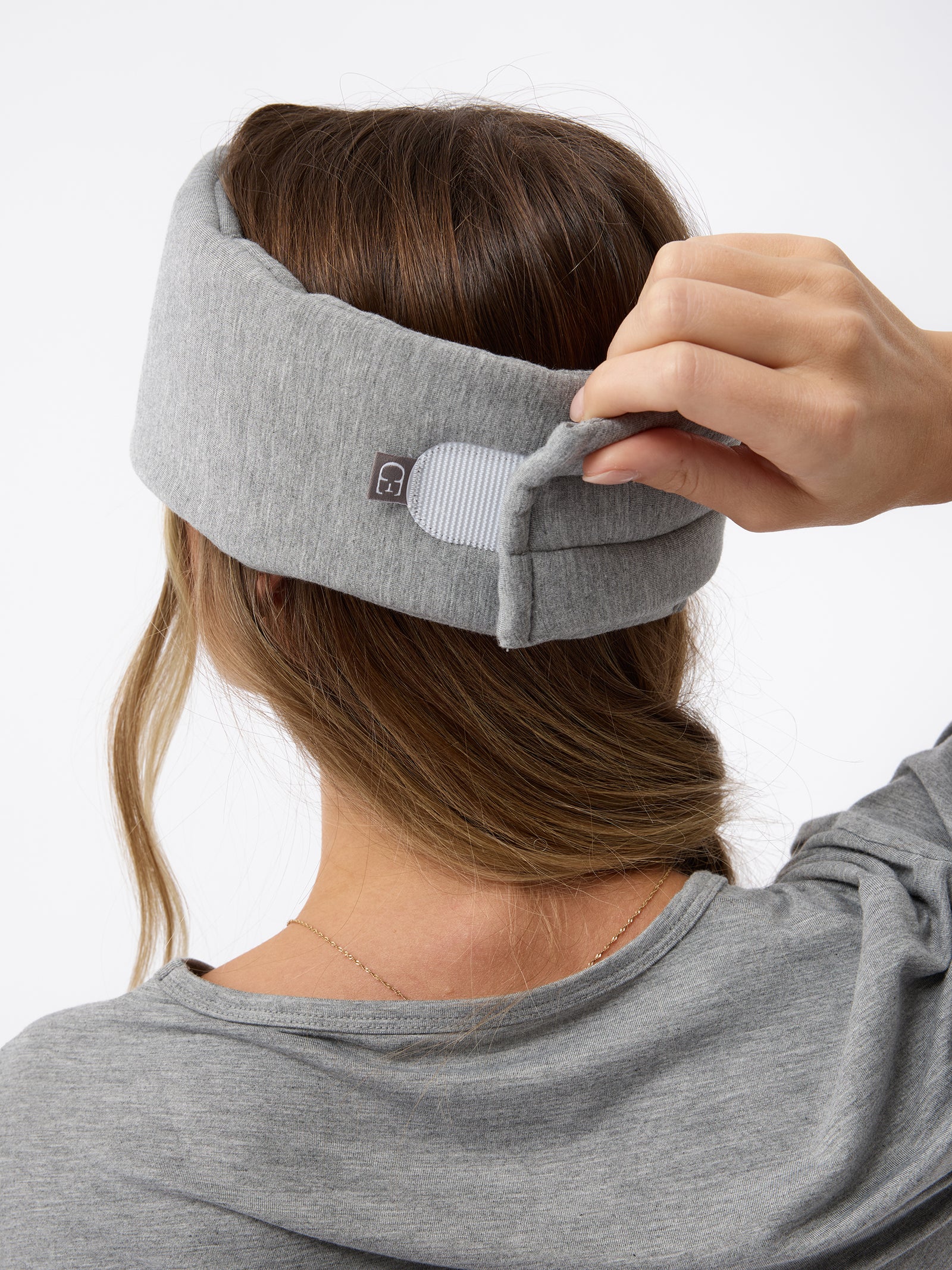 A woman wears the Cozy Earth Adjustable Bamboo Sleep Mask in Grey. She is facing away and showing where the mask fastens at the back. 