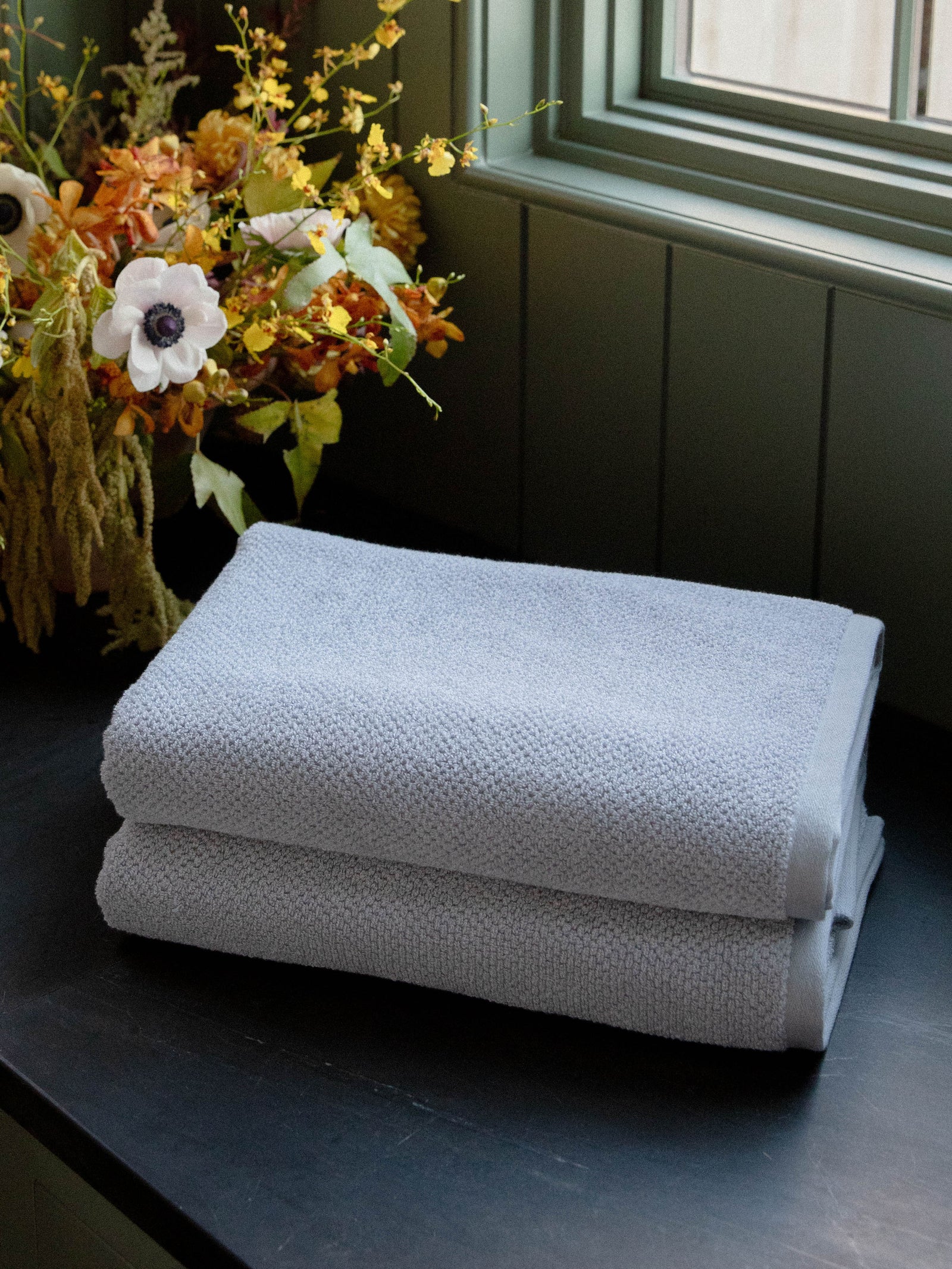 Nantucket Bath Towels in the color Heathered Harbor Mist. Photo of Nantucket Bath Towels taken with the bath towels resting on a countertop in a bathroom. 