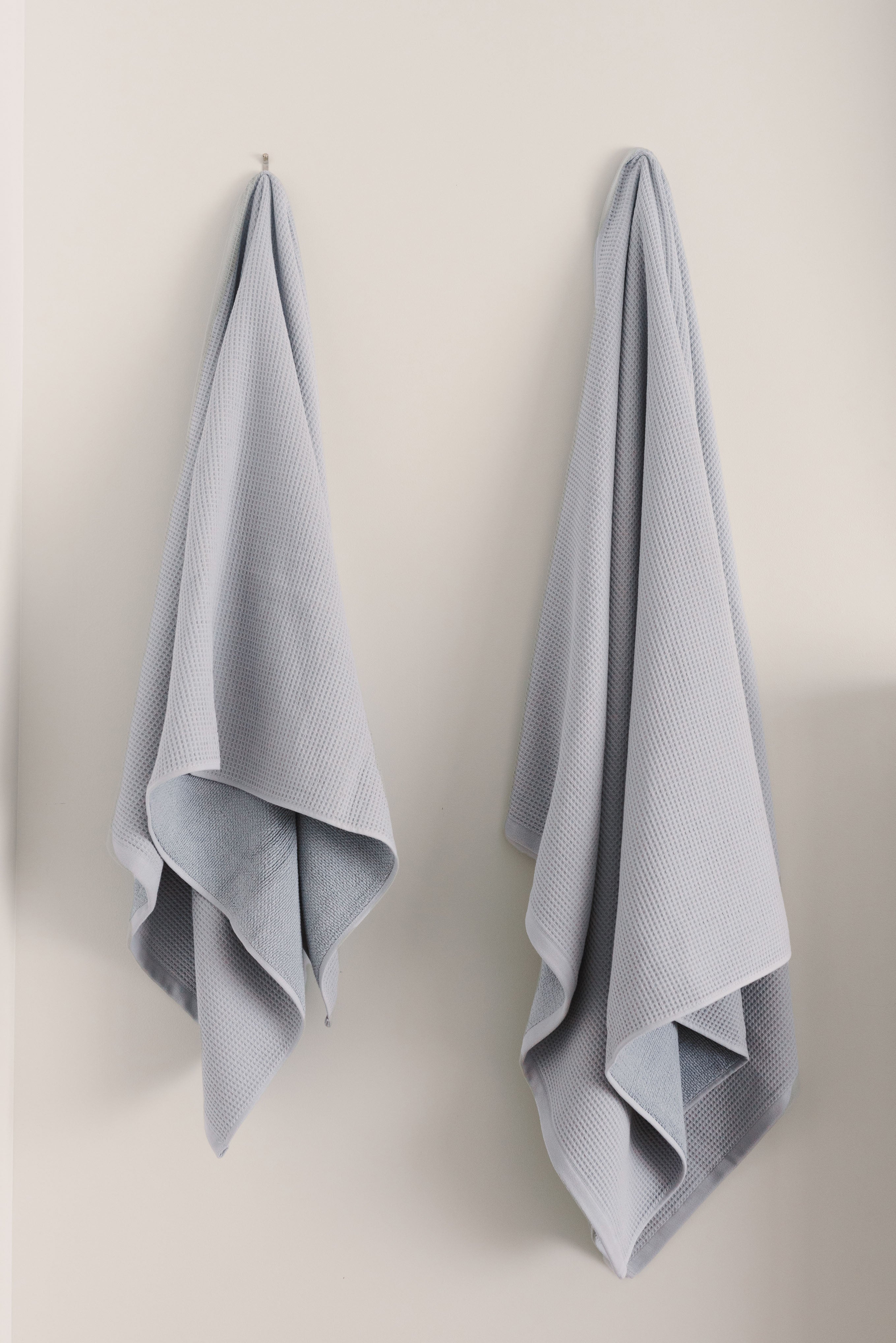 Waffle Bath Towel in the color Harbor Mist. Photo of Harbor Mist Waffle Bath Towel taken hanging from a towel hook in a white bathroom. |Color: Harbor Mist