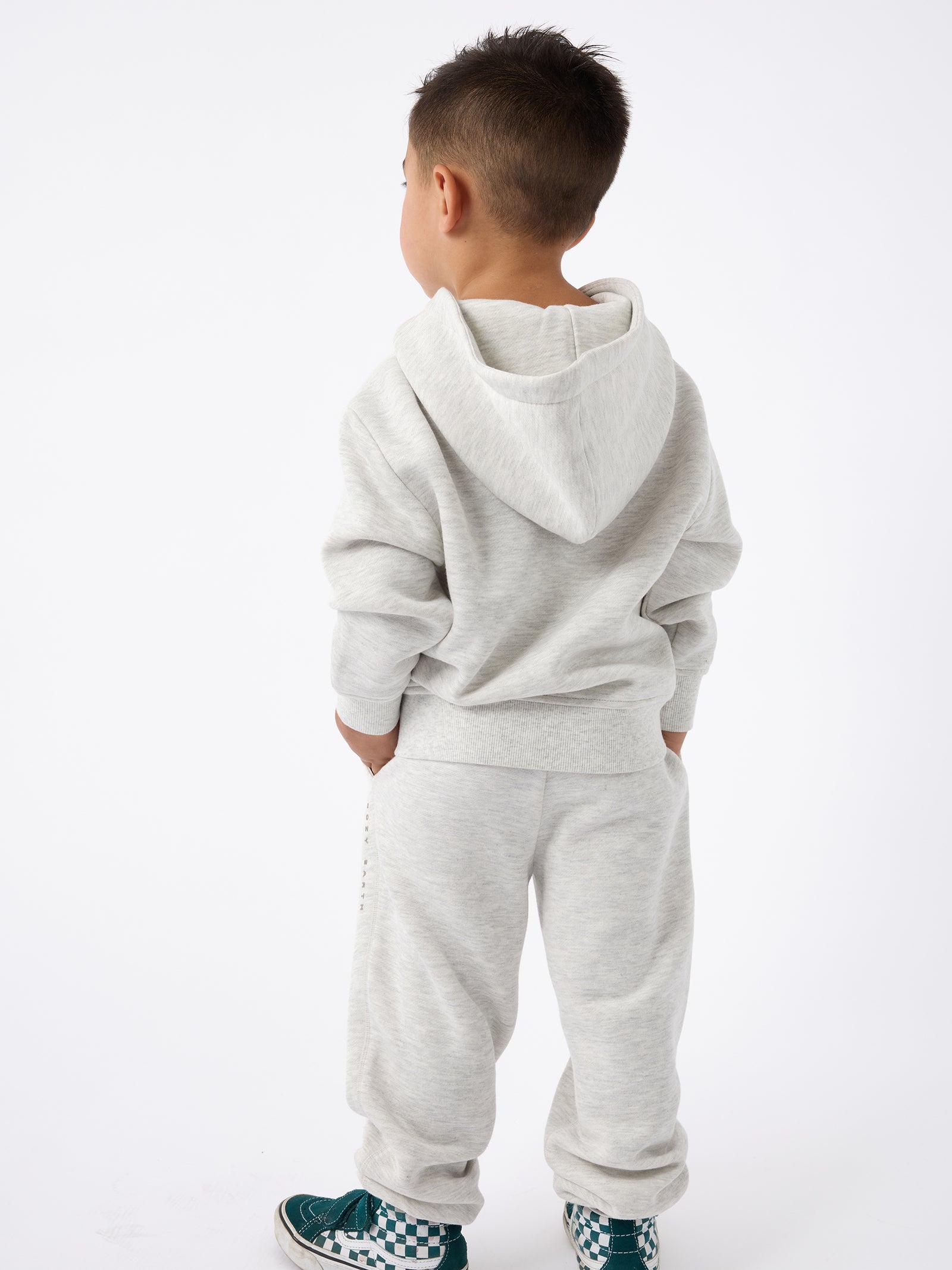 A young child facing away, dressed in a Kid's CityScape Hoodie by Cozy Earth and sweatpants. The child is also wearing teal and white checkered sneakers against a plain white background. 