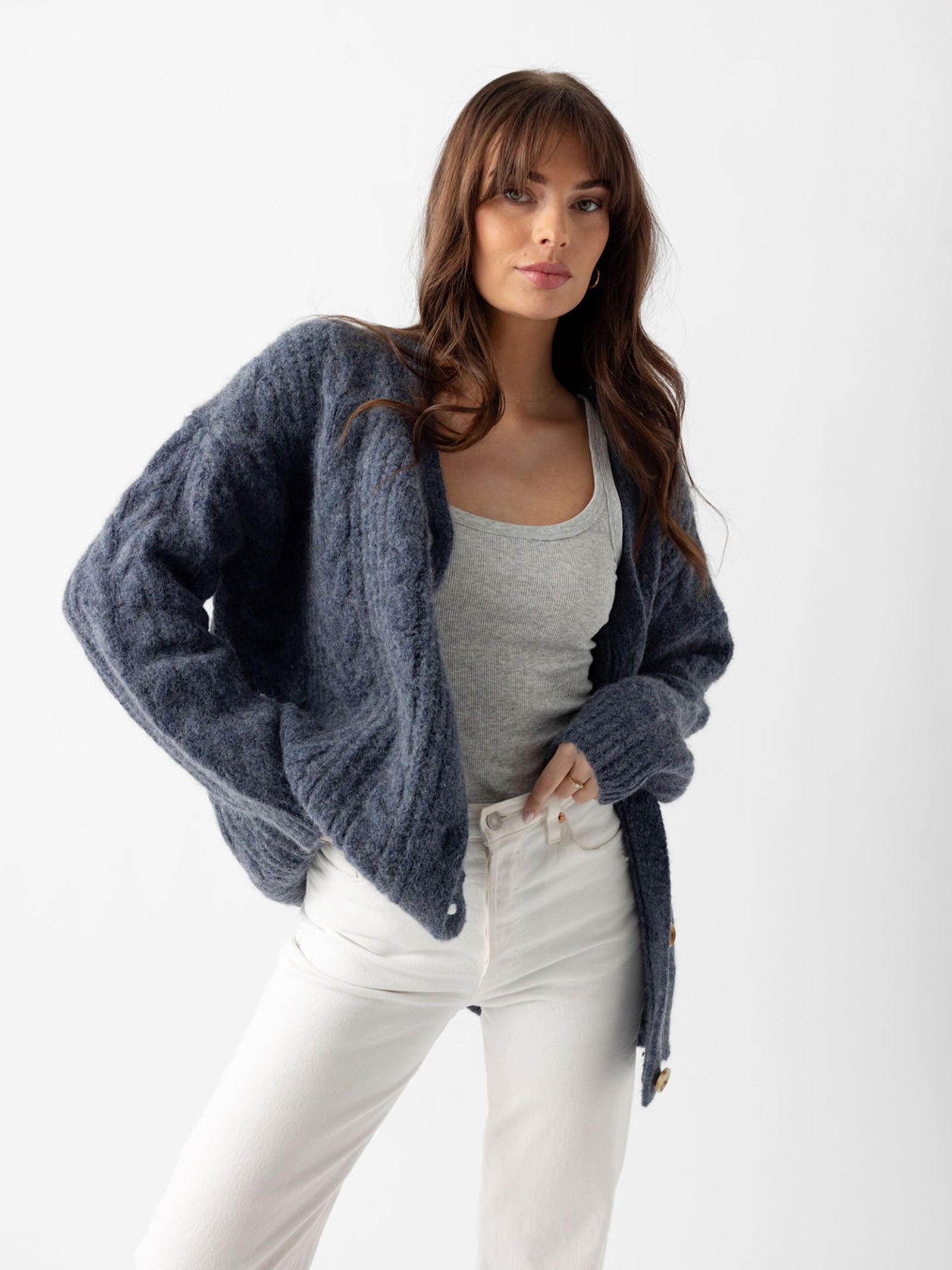 Woman wearing indigo cardigan over grey tank and white pants with white background 