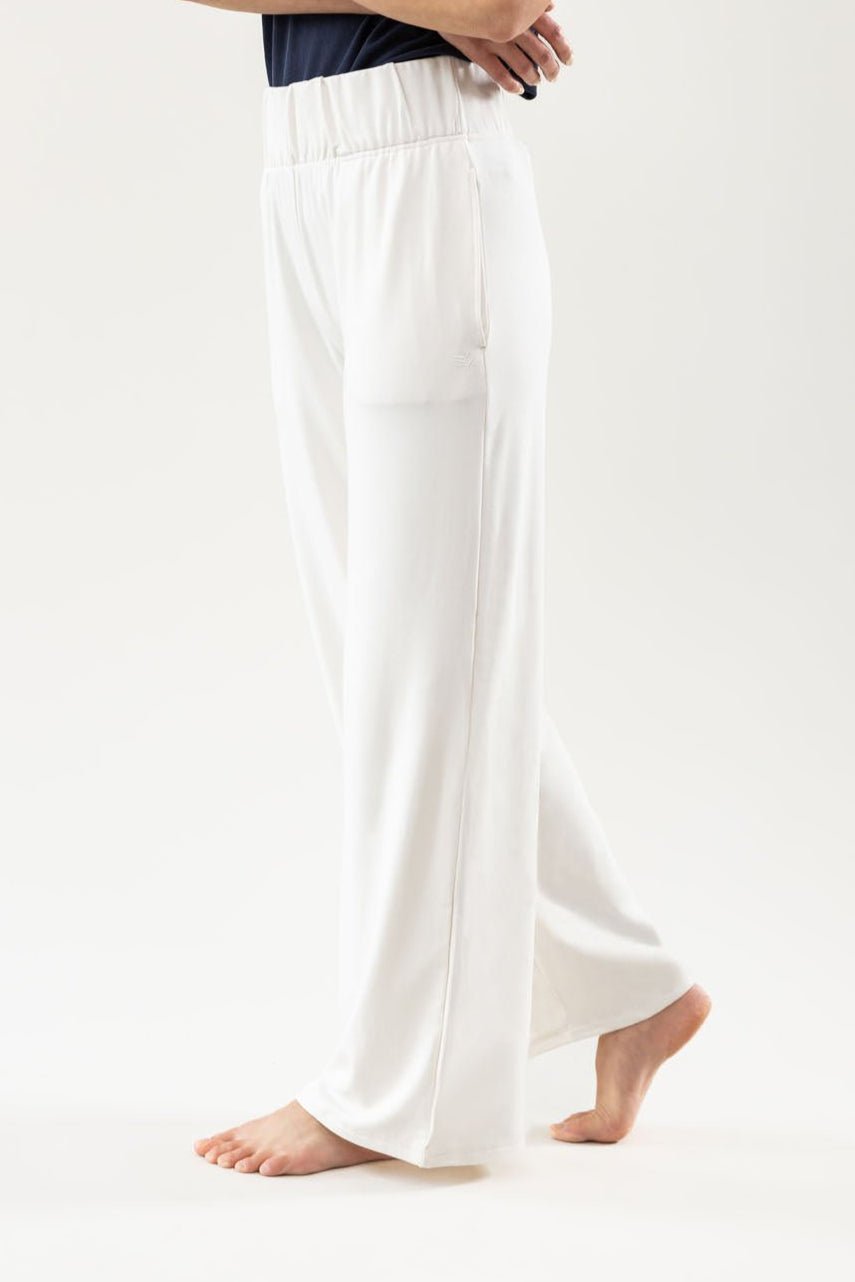 A person wearing the Cozy Earth Women's Ultra-Soft Bamboo Wide Leg Pull On Pant & Pullover Set stands barefoot with arms crossed against a plain light background. |Color:Ivory