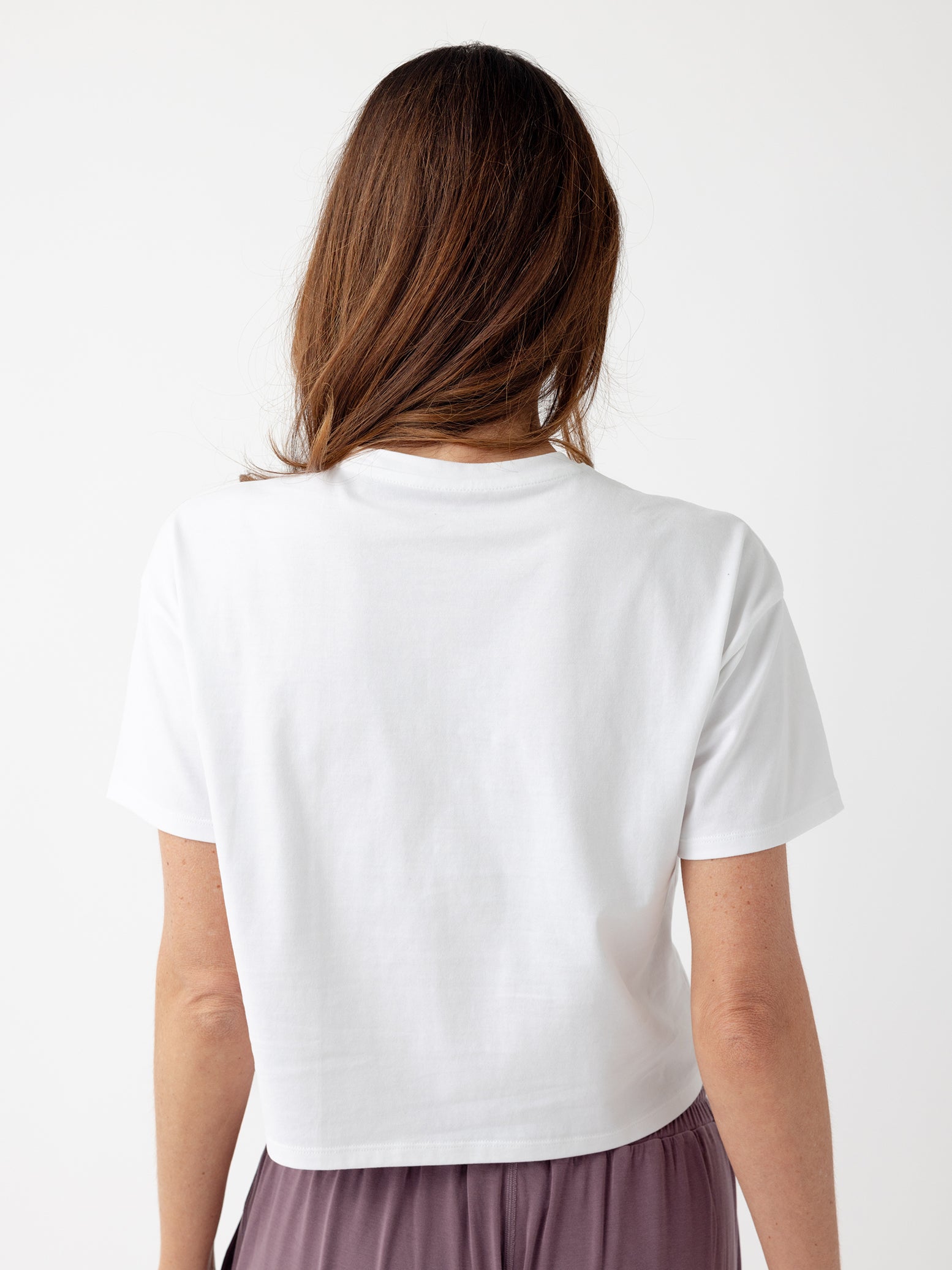 White All Day Cropped Tee. The photo of the All Day Cropped Tee is taken with a with a white background and is worn by a woman. 