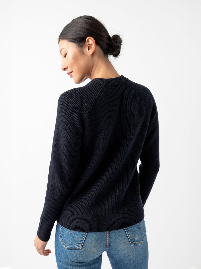 A person with dark hair styled in a low bun is wearing the Women's Classic Crewneck by Cozy Earth and blue jeans, standing with their back facing the camera. The background is white and plain.