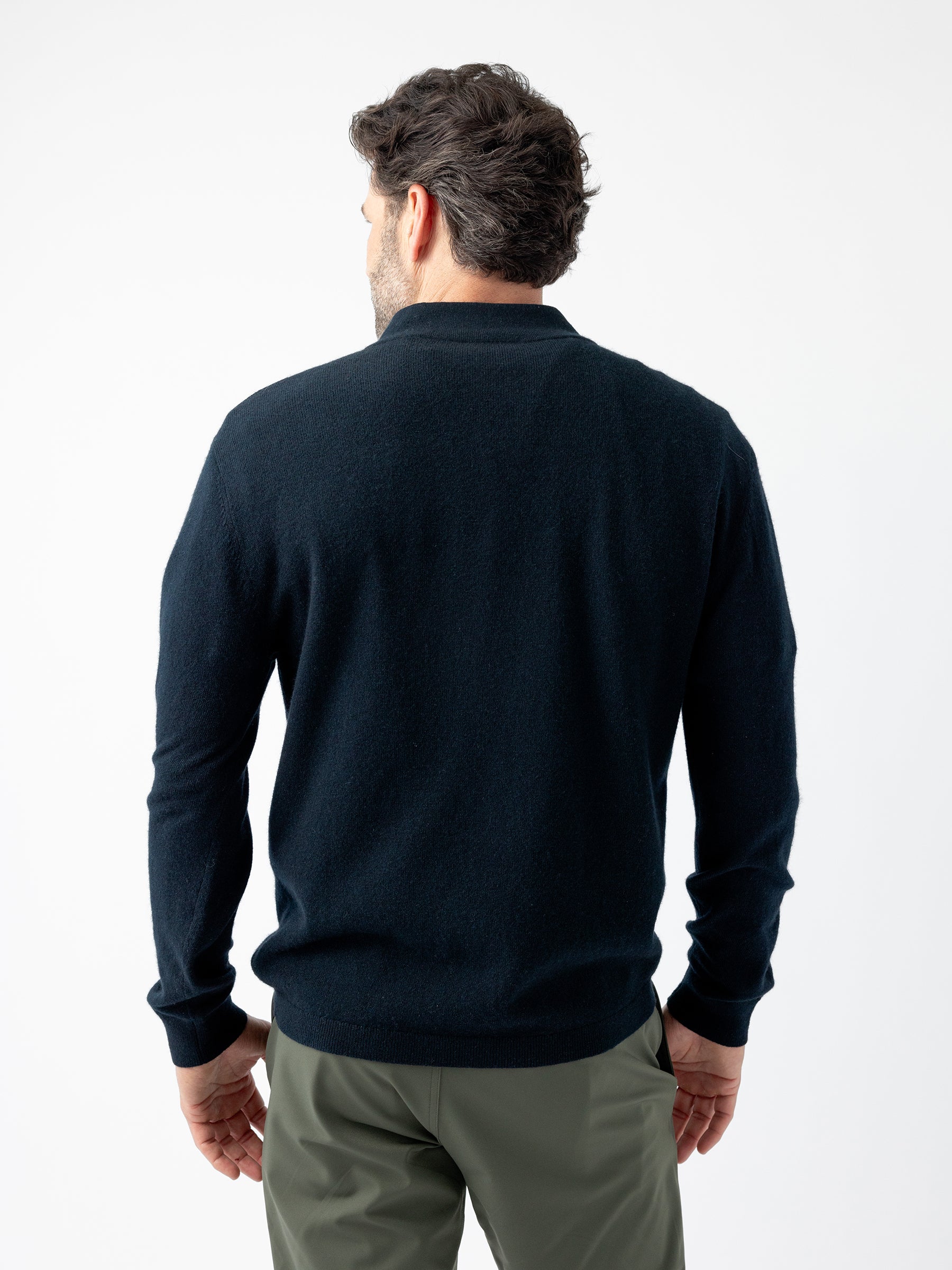 A man with short dark hair is seen from the back, wearing a long-sleeved, dark blue Men's Quarter Zip Sweater by Cozy Earth and olive green pants. He stands against a plain white background. |Color:Jet Black