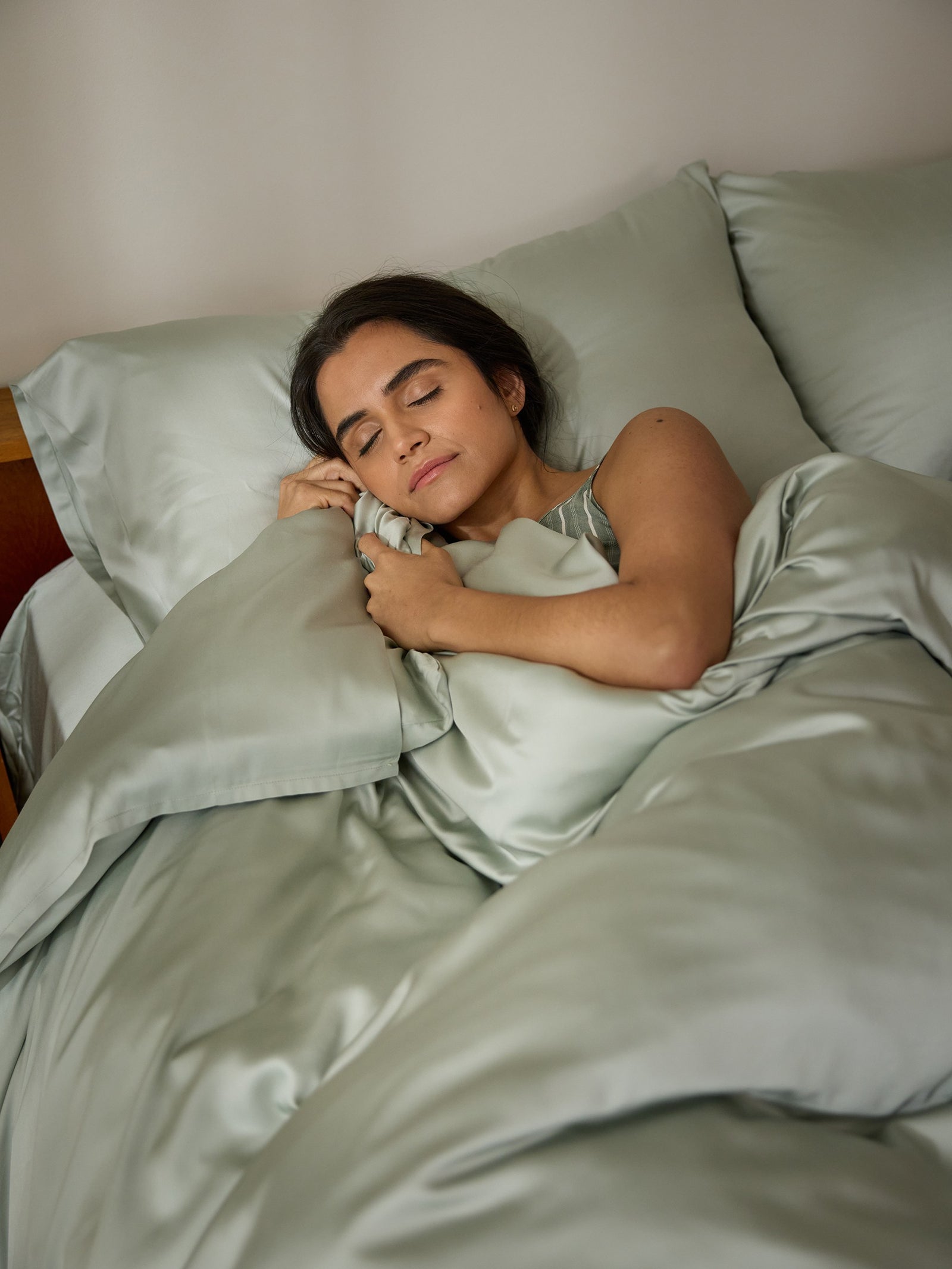 A woman peacefully sleeps in a bed with a Cozy Earth Bamboo Duvet Cover and matching pillowcases, clutching one pillow close. The setting conveys comfort and tranquility. 