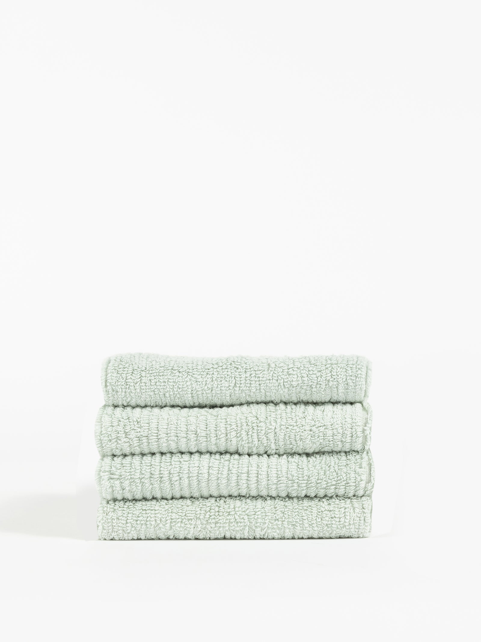 A stack of four neatly folded, Cozy Earth Ribbed Terry Washcloths in light green is placed against a plain white background. The texture of these washcloths appears soft and plush, with visible ribbed detailing in the fabric. The overall look is clean and minimalistic. 