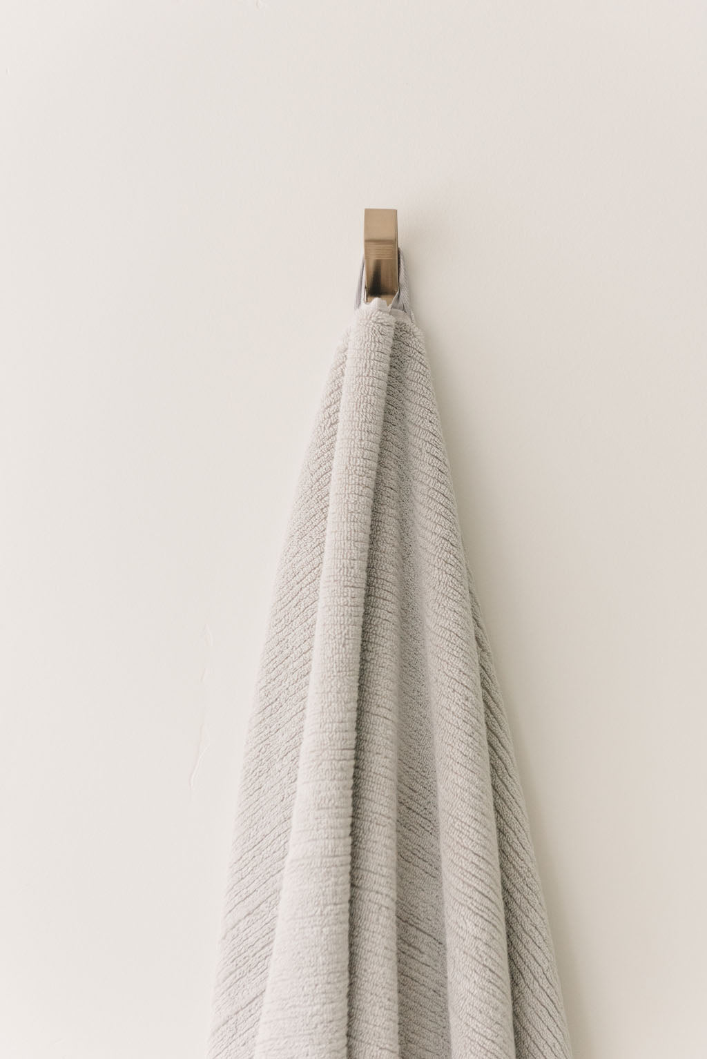 Ribbed Terry Bath Towel in the color Light Grey. Photo of Ribbed Terry Bath Towel taken as the Light Grey Ribbed Terry Bath Towel is hanging from a towel hook in a bathroom. 